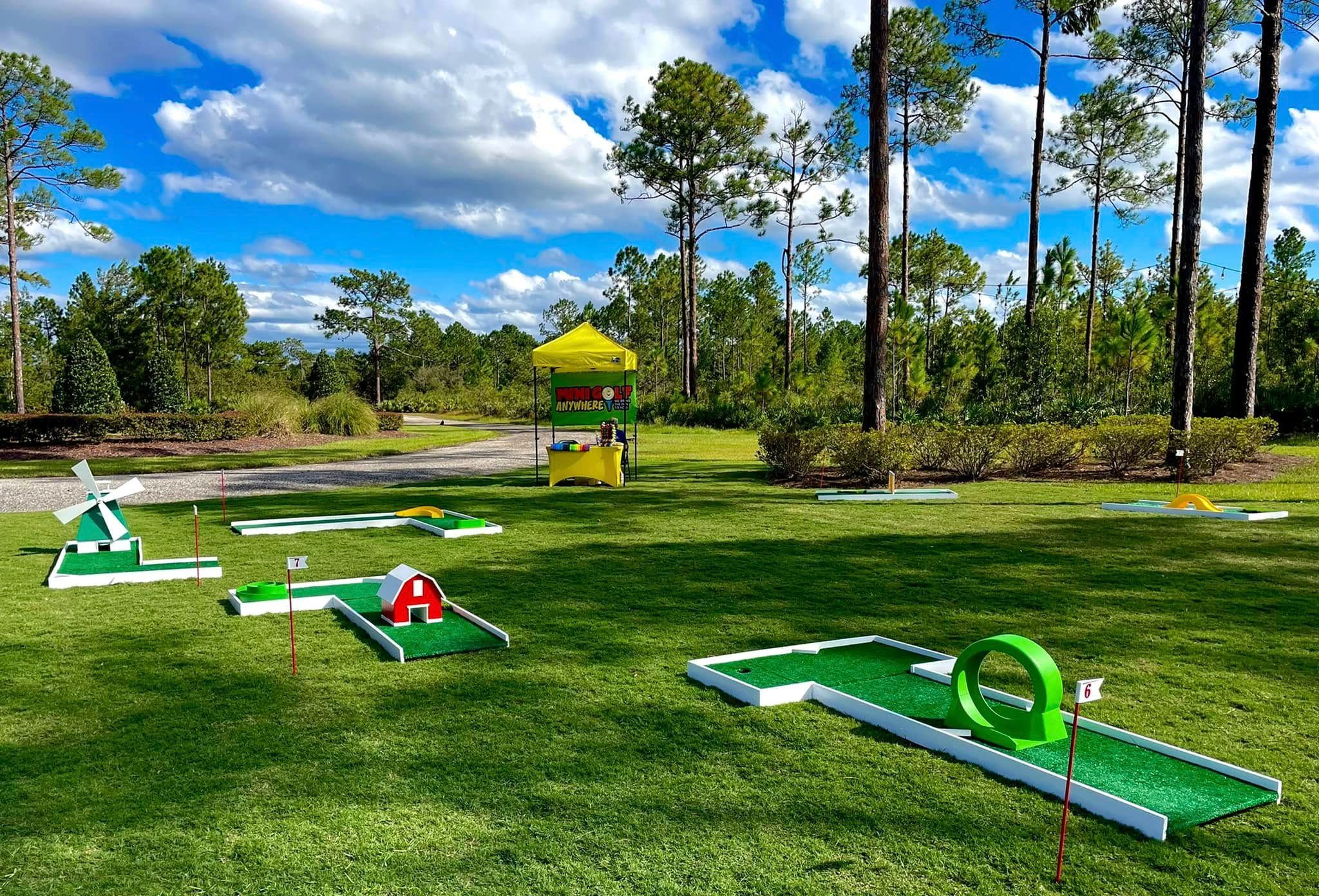 several portable mini golf holes and a shade canopy set up on an open field in Orlando