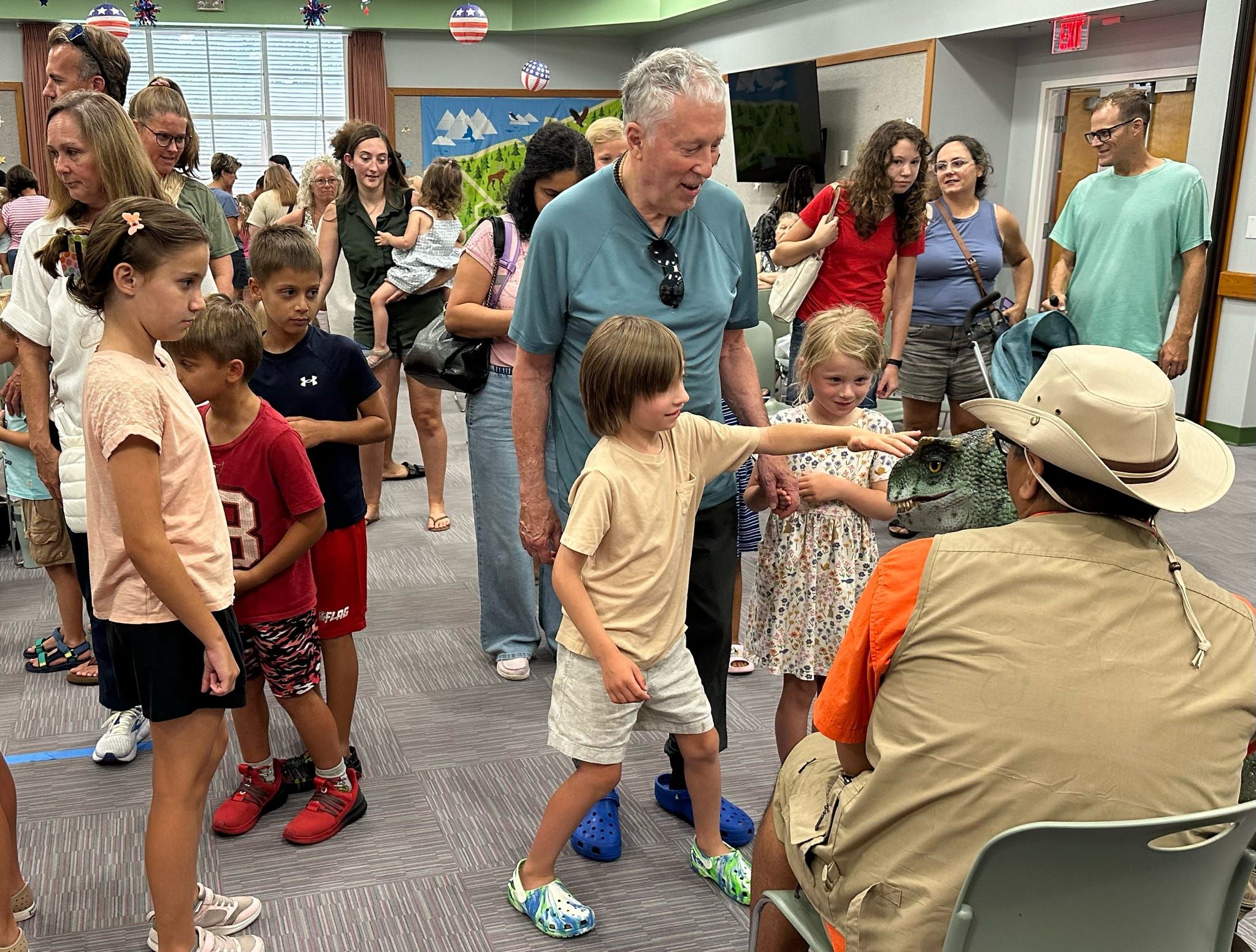 Kids crowd around a trainer to meet a lifelike baby T. rex