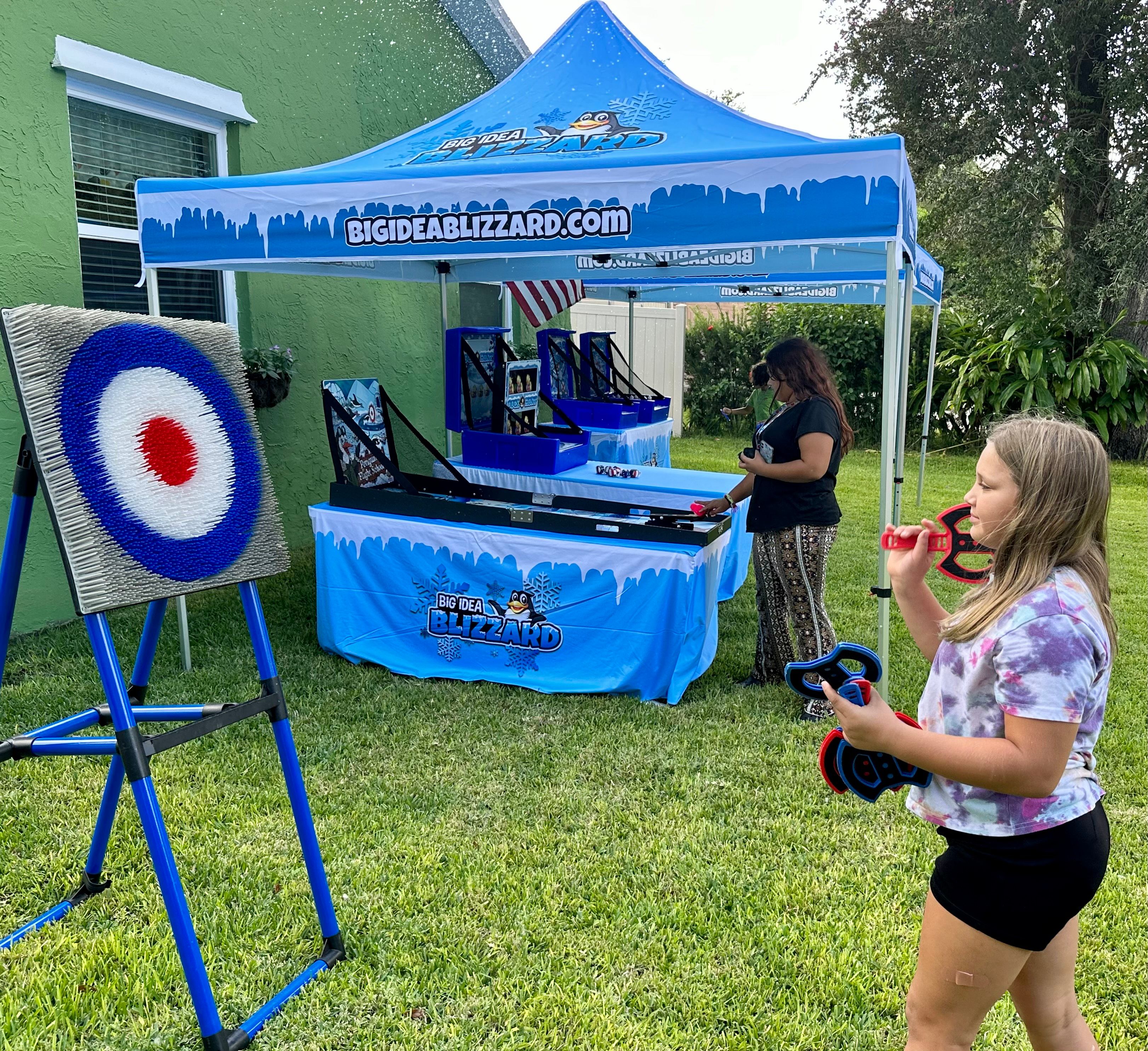 A girl holds soft throwing axes at the axe-throw target under a Blizzard tent