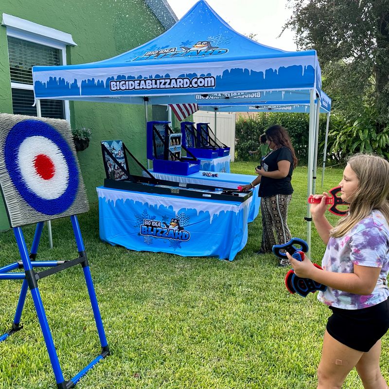 A girl holds soft throwing axes at the axe-throw target under a Blizzard tent