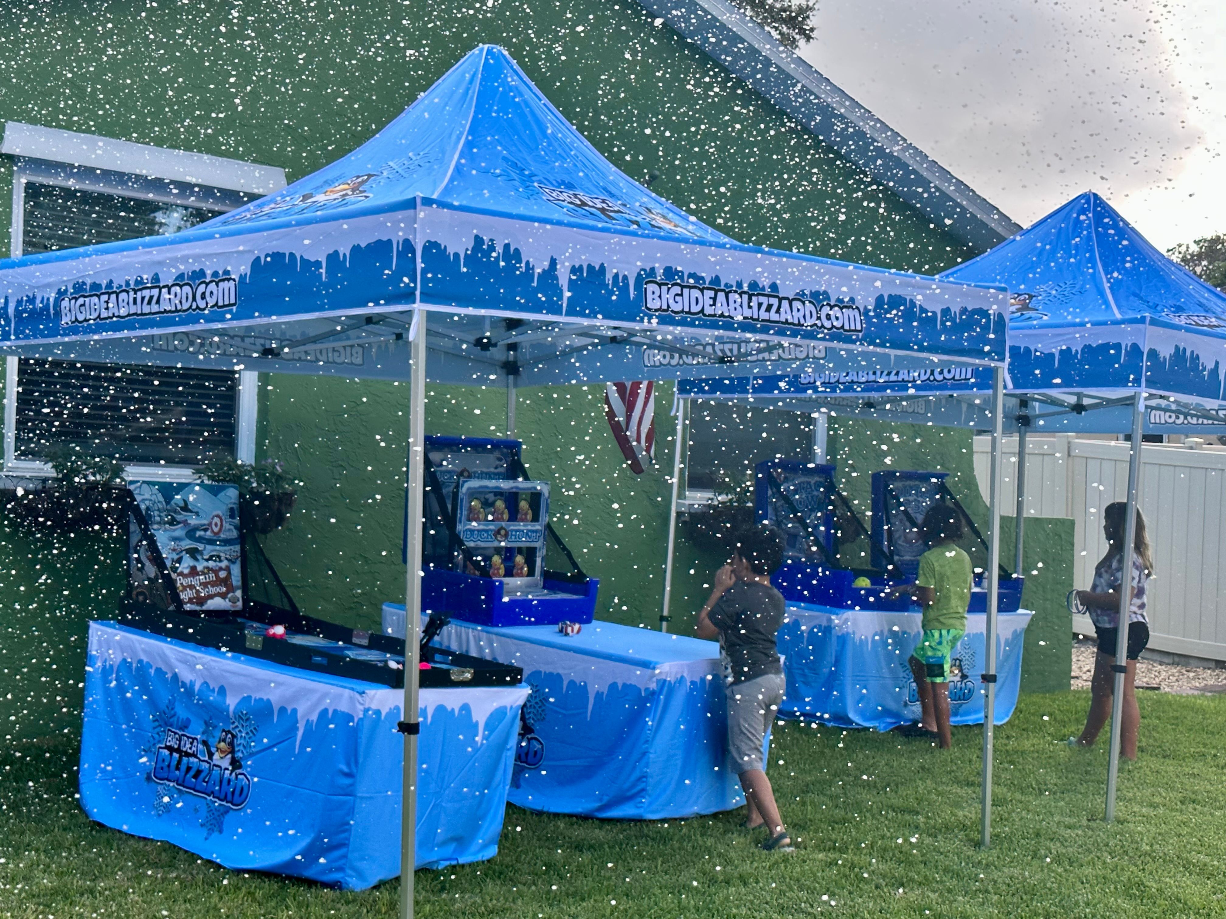 Two Big Idea Blizzard tents with winter games on a lawn, with snow falling over kids at play