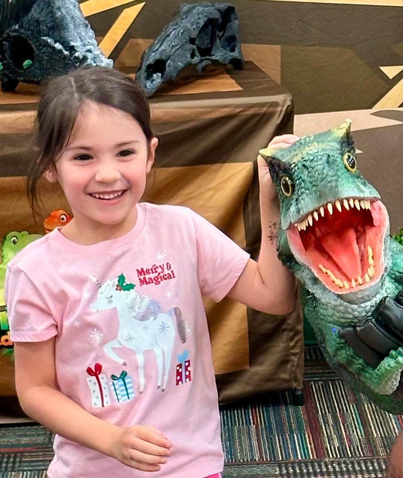 A smiling girl stands cheek to cheek with a lifelike baby T. rex