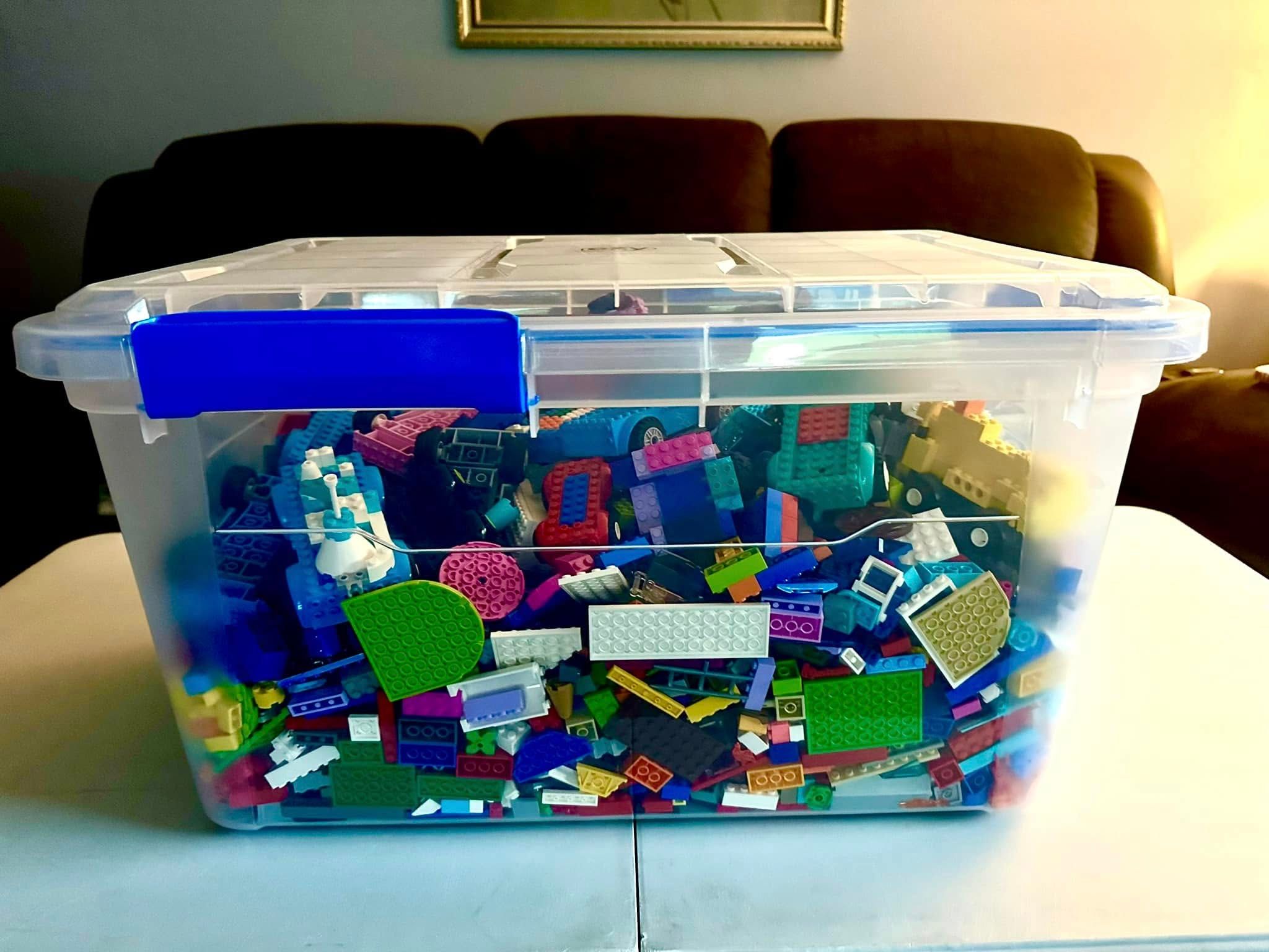A clear storage bin filled to the lid with building bricks and brick-built cars