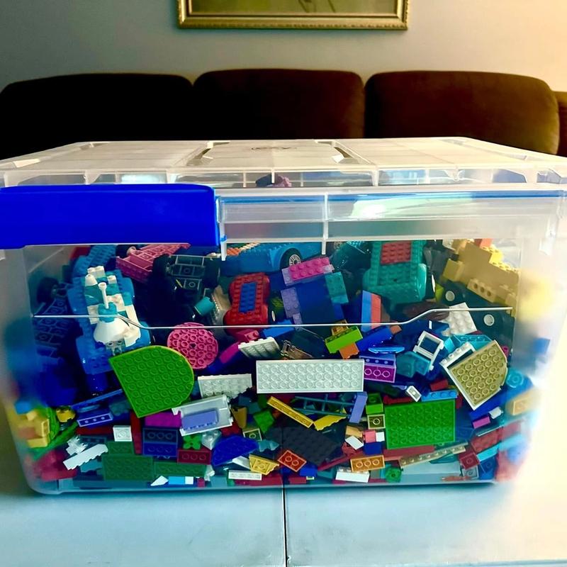 A clear storage bin filled to the lid with building bricks and brick-built cars