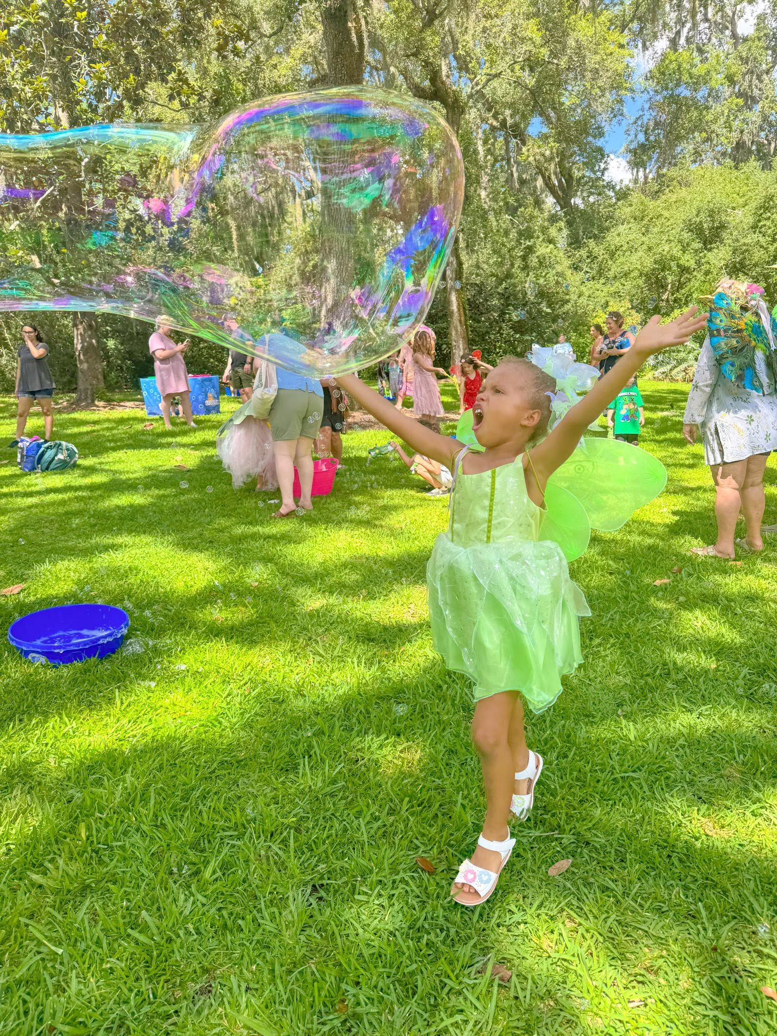 a girl in a green dress reaching up for a giant bubble on a lawn