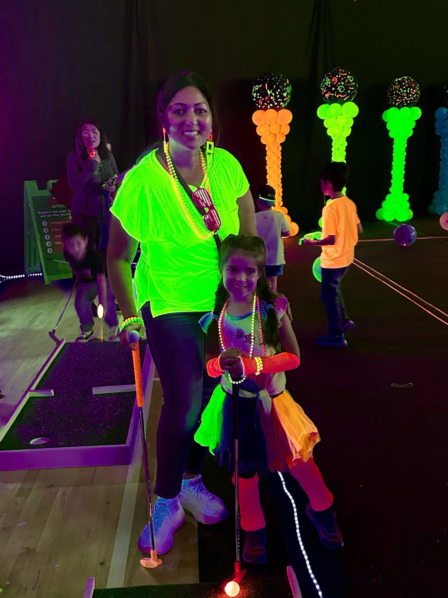 guests in glow accessories gathered around a blacklit mini golf hole