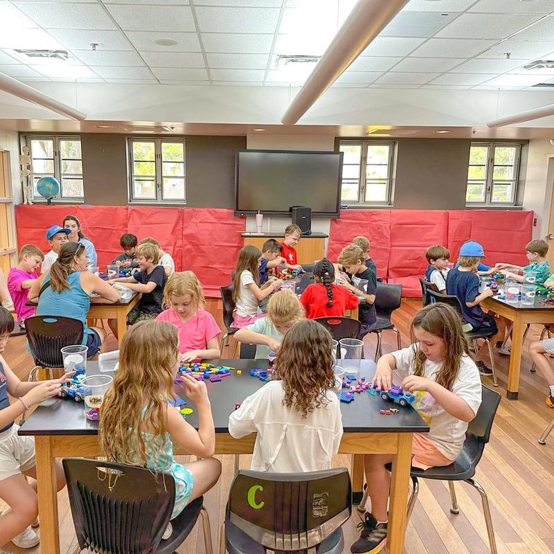 A room full of kids builds with bricks at classroom tables during a Brick Lab session