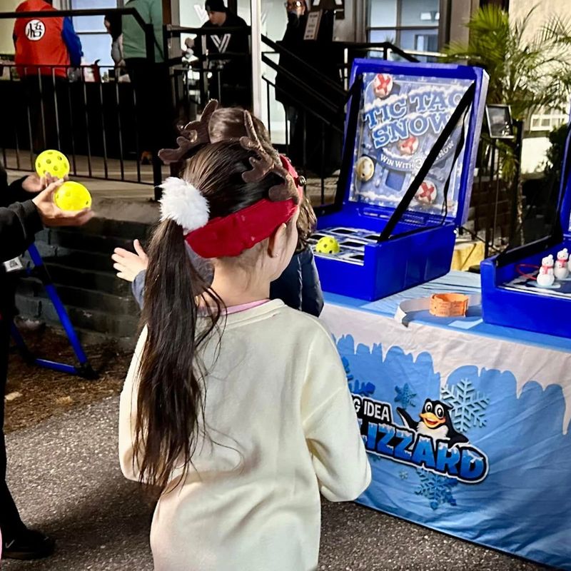 Kids in reindeer antlers wait as an attendant hands out balls for Tic Tac Snow at a Blizzard table