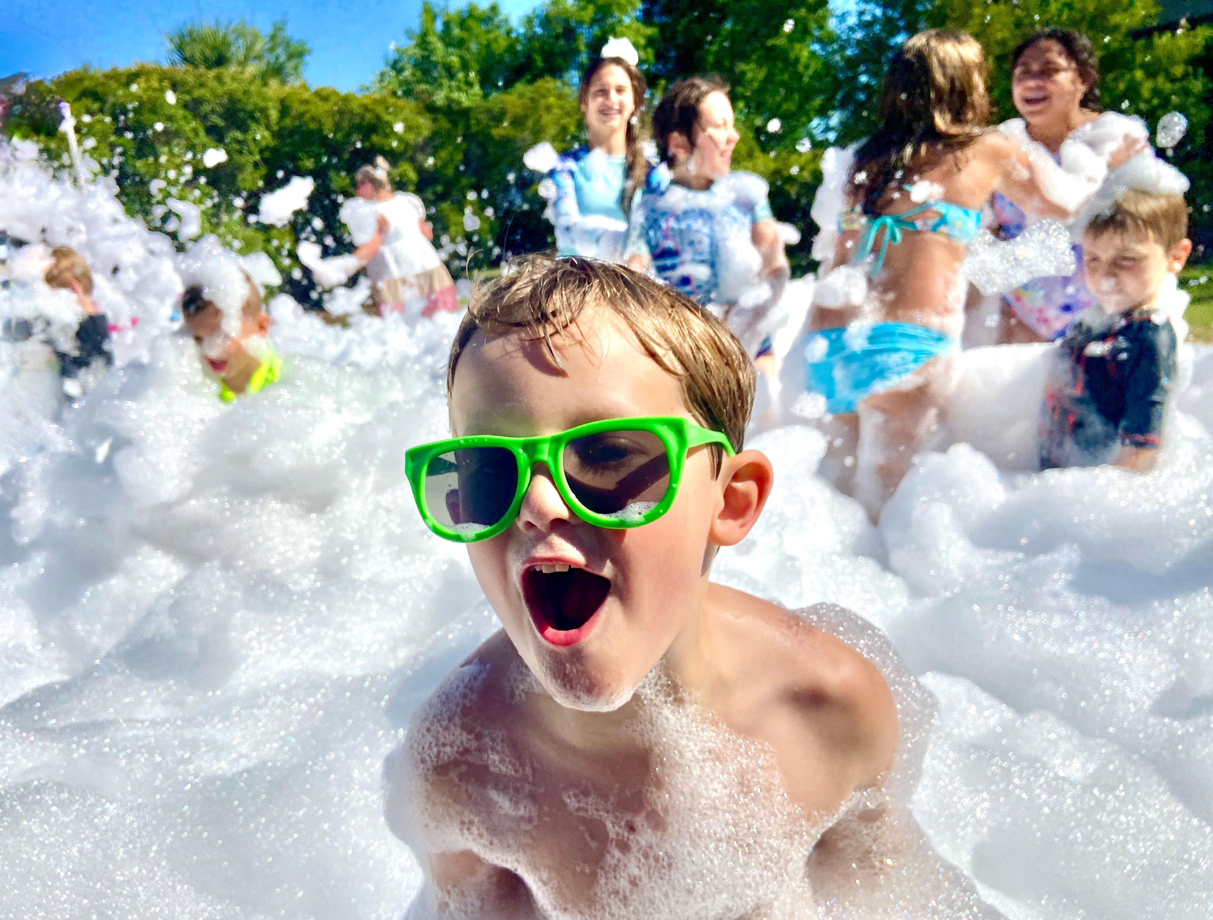 Children laughing while running through foam at a backyard birthday party