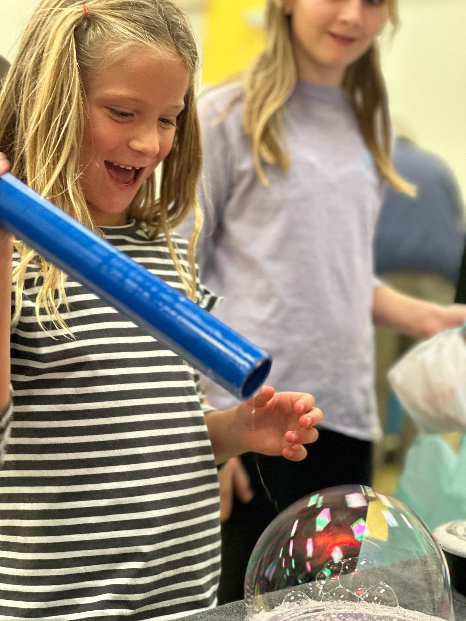 a girl watching a bubble form on the end of a blue wand