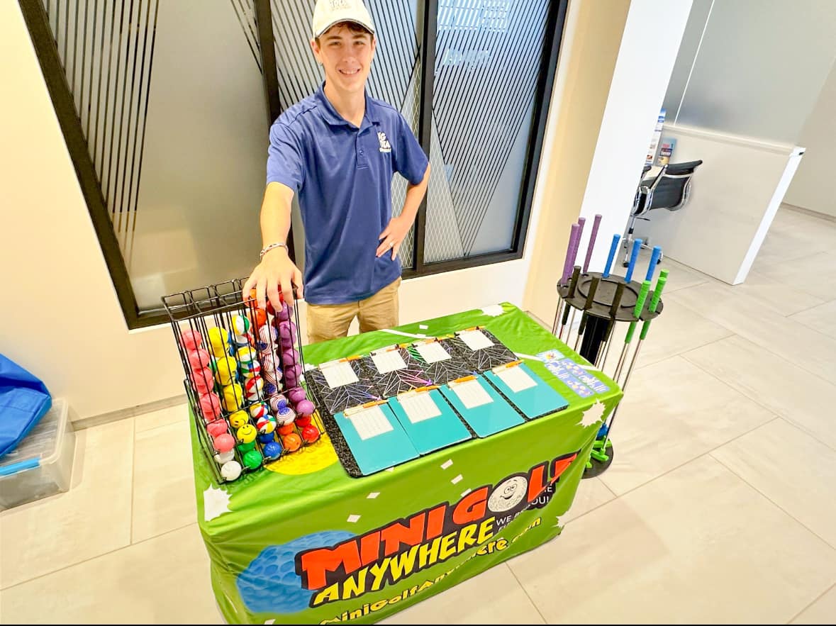 a staffer behind the branded mini golf club cart stocked with putters and balls