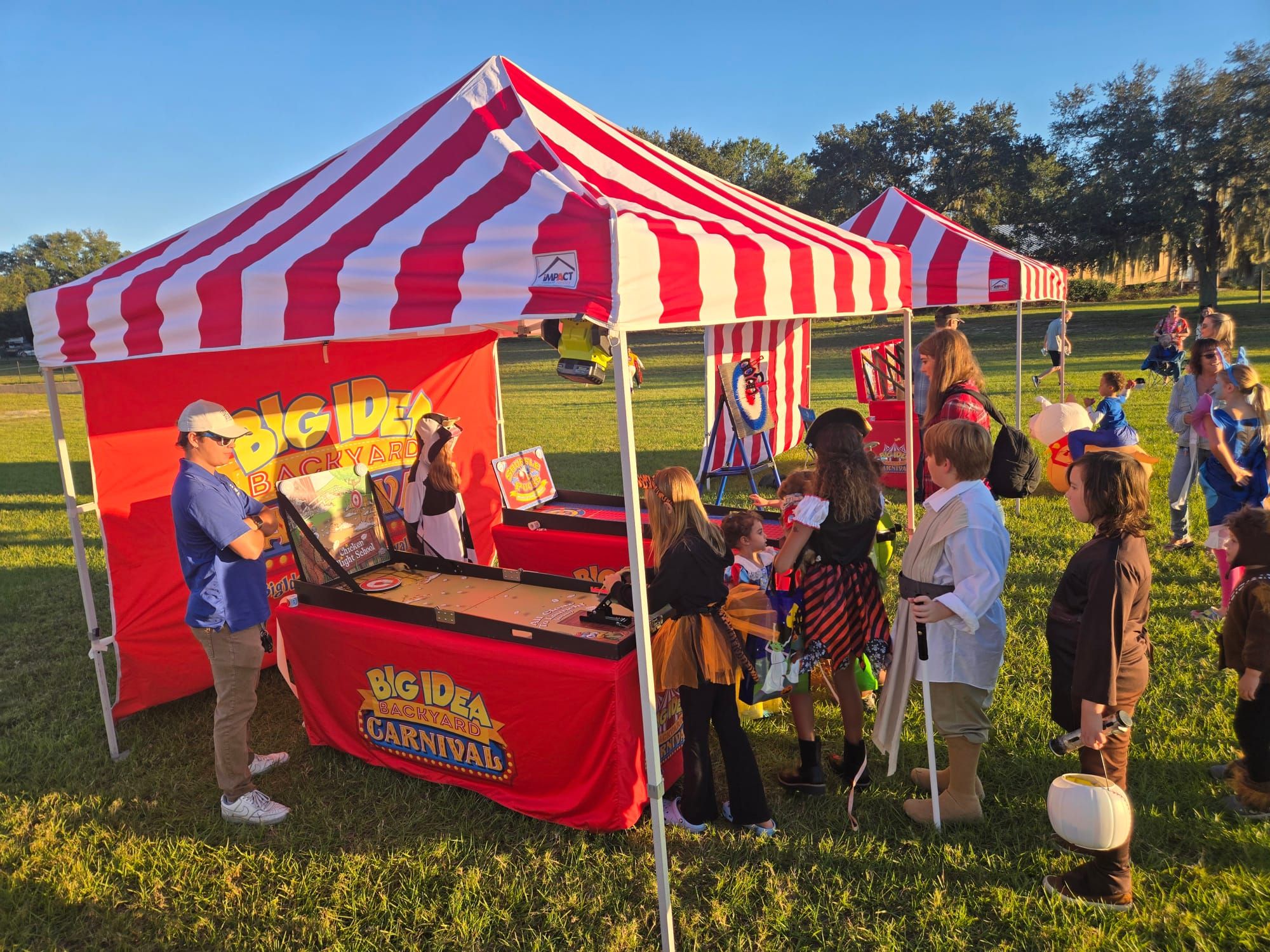 A striped carnival tent with kids lined up at a game booth.