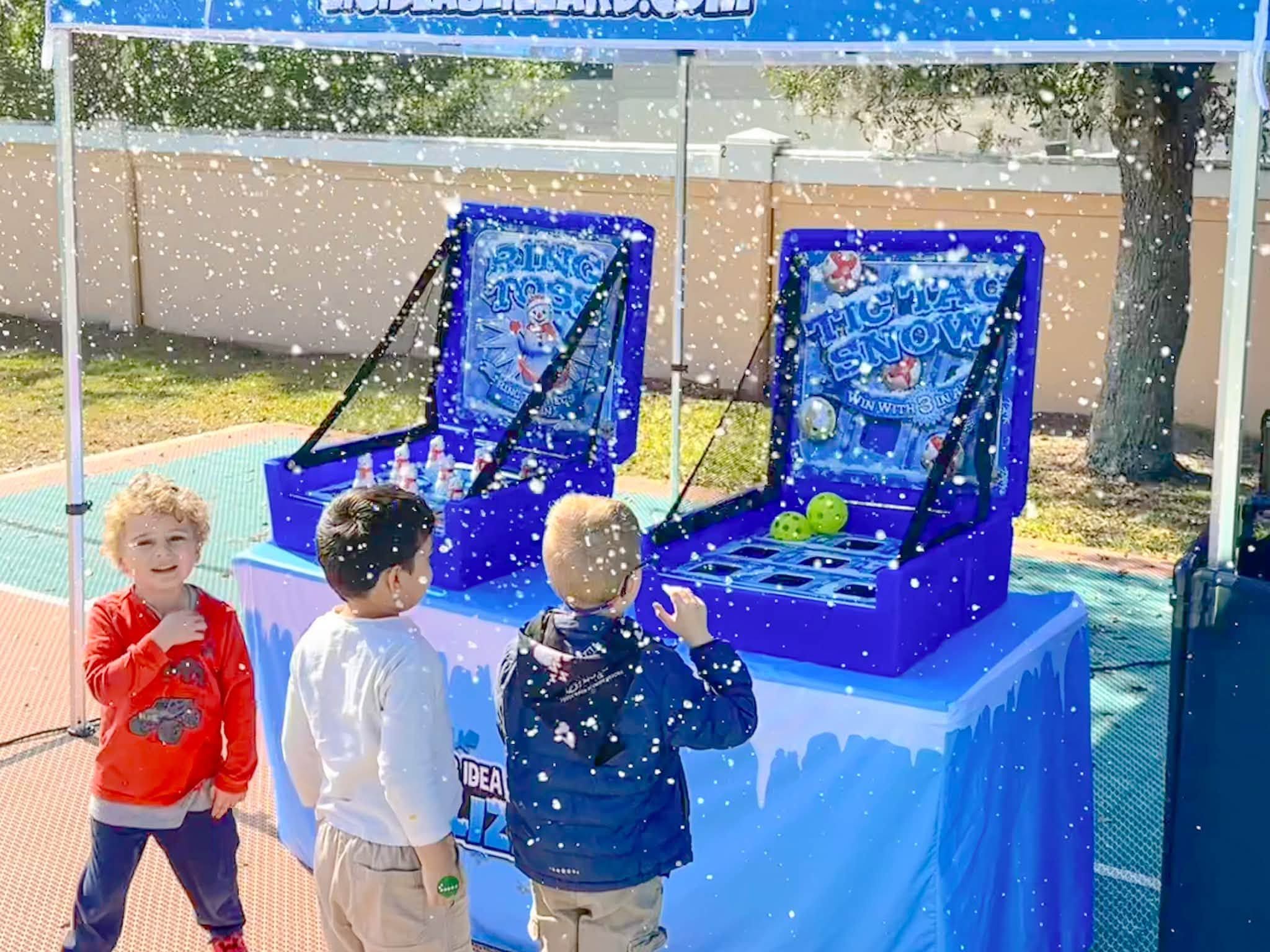 Three boys play Ring Toss and Tic Tac Snow under a Blizzard tent as snow falls around them