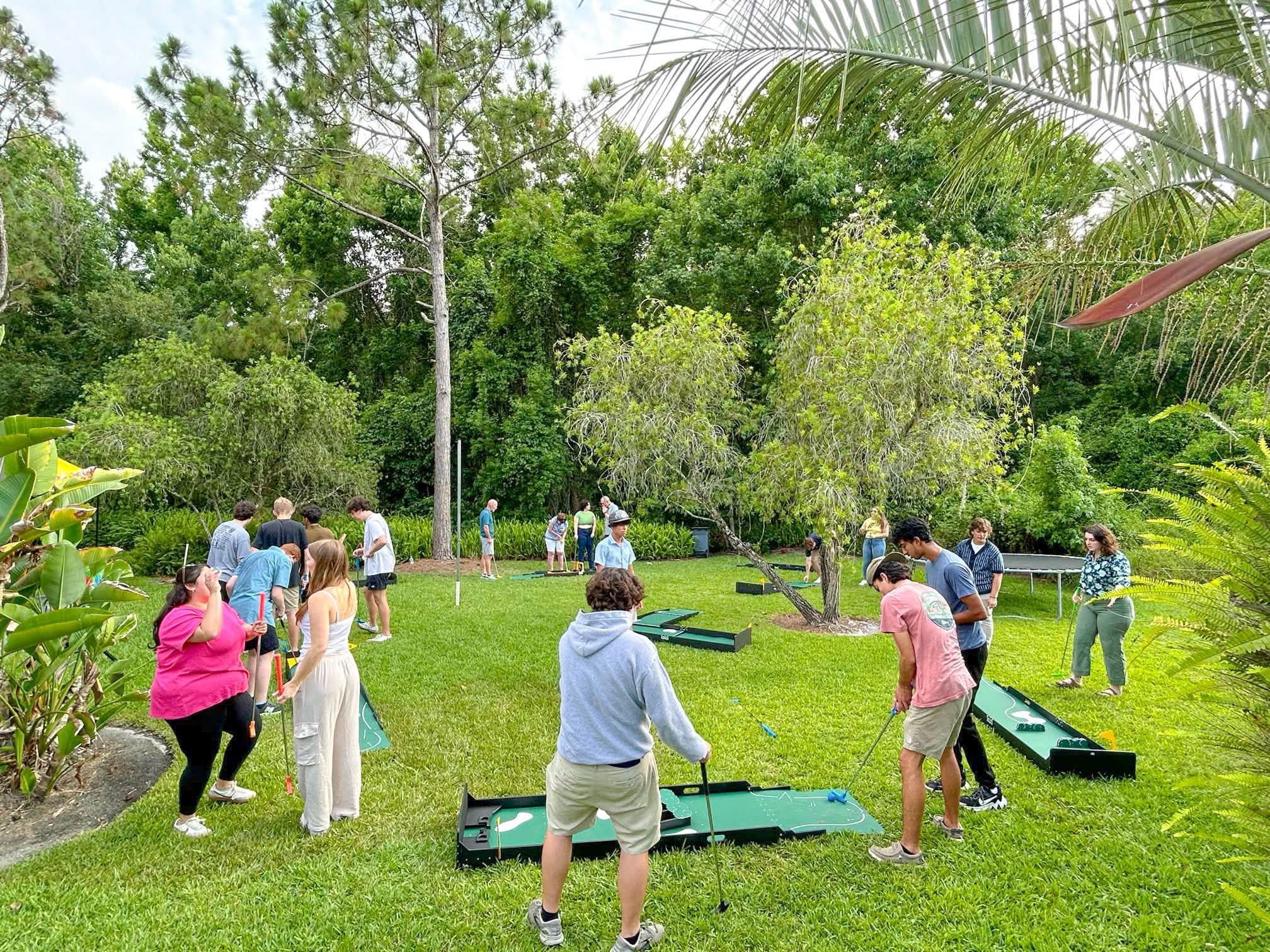 a group of adults and kids playing a portable mini golf course on a park lawn in Atlanta
