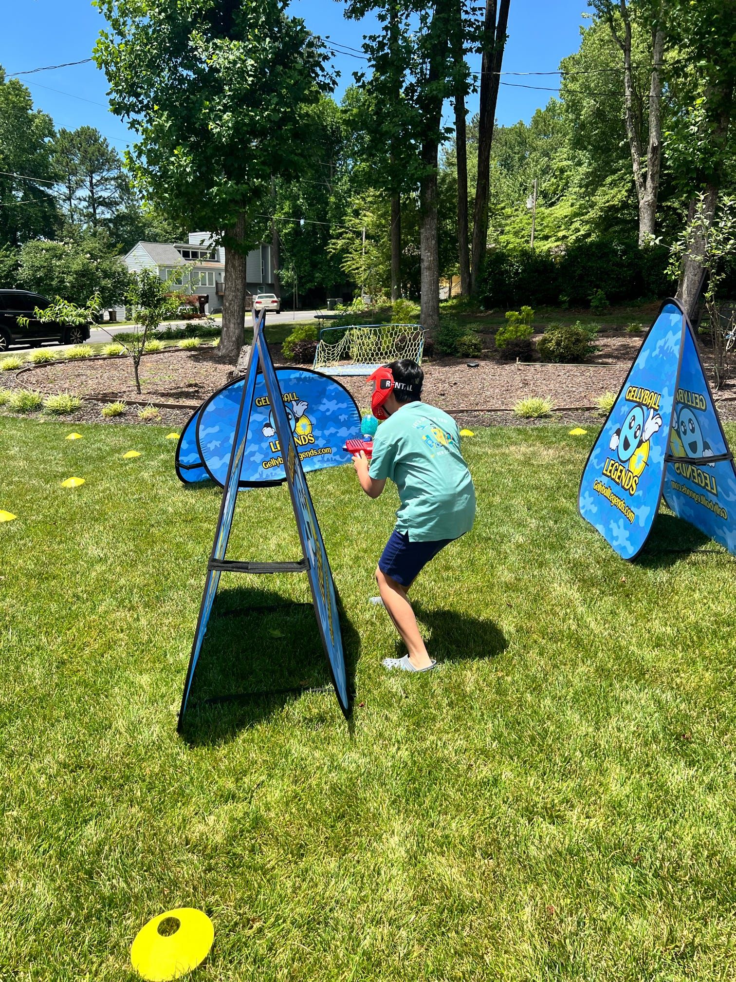 A boy in a red mask crouches behind an A-frame bunker on a backyard lawn