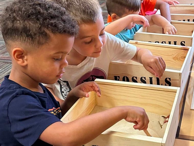 Kids brush through the sand of a fossil dig box