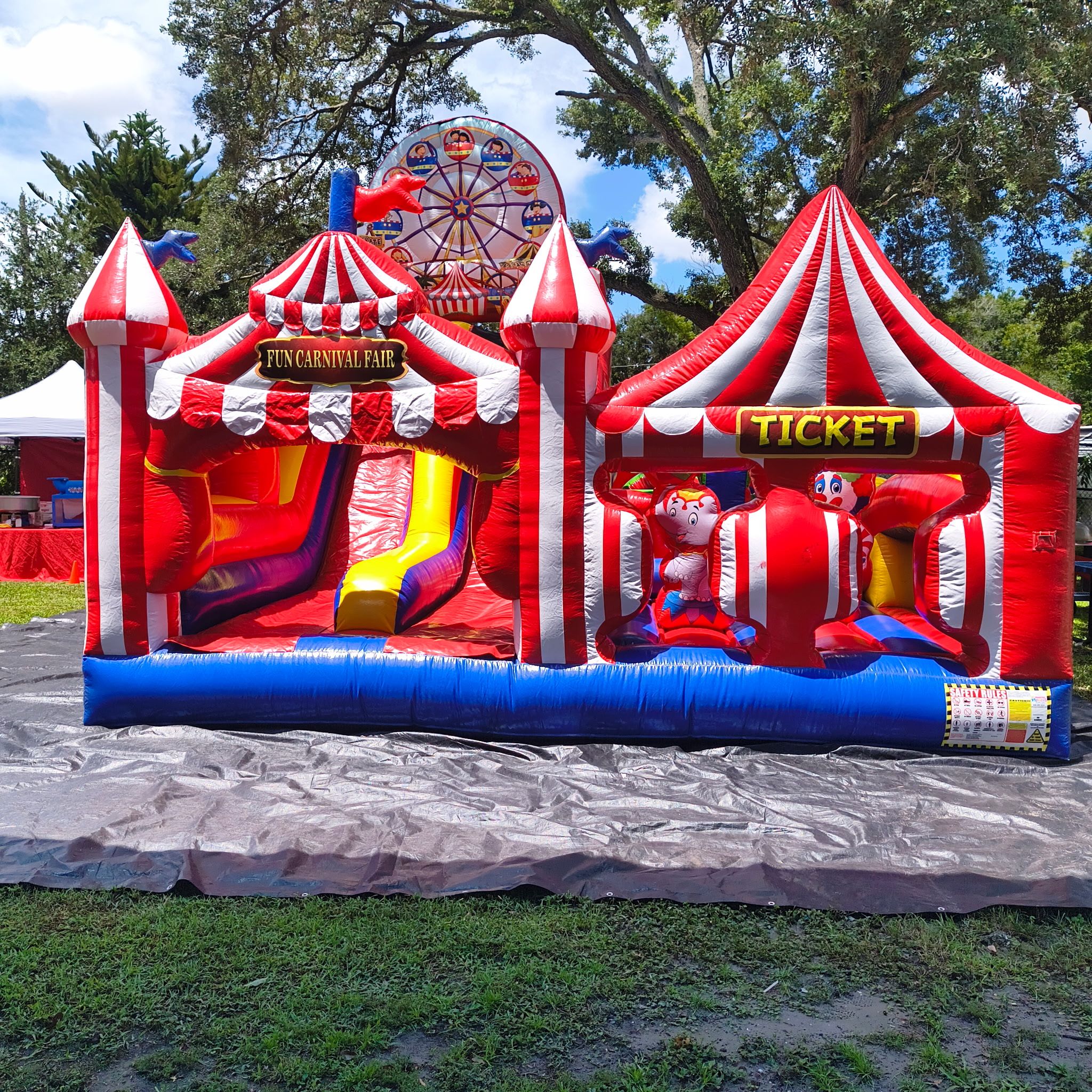 an inflatable carnival obstacle course with a slide and a ticket booth set up on a lawn.