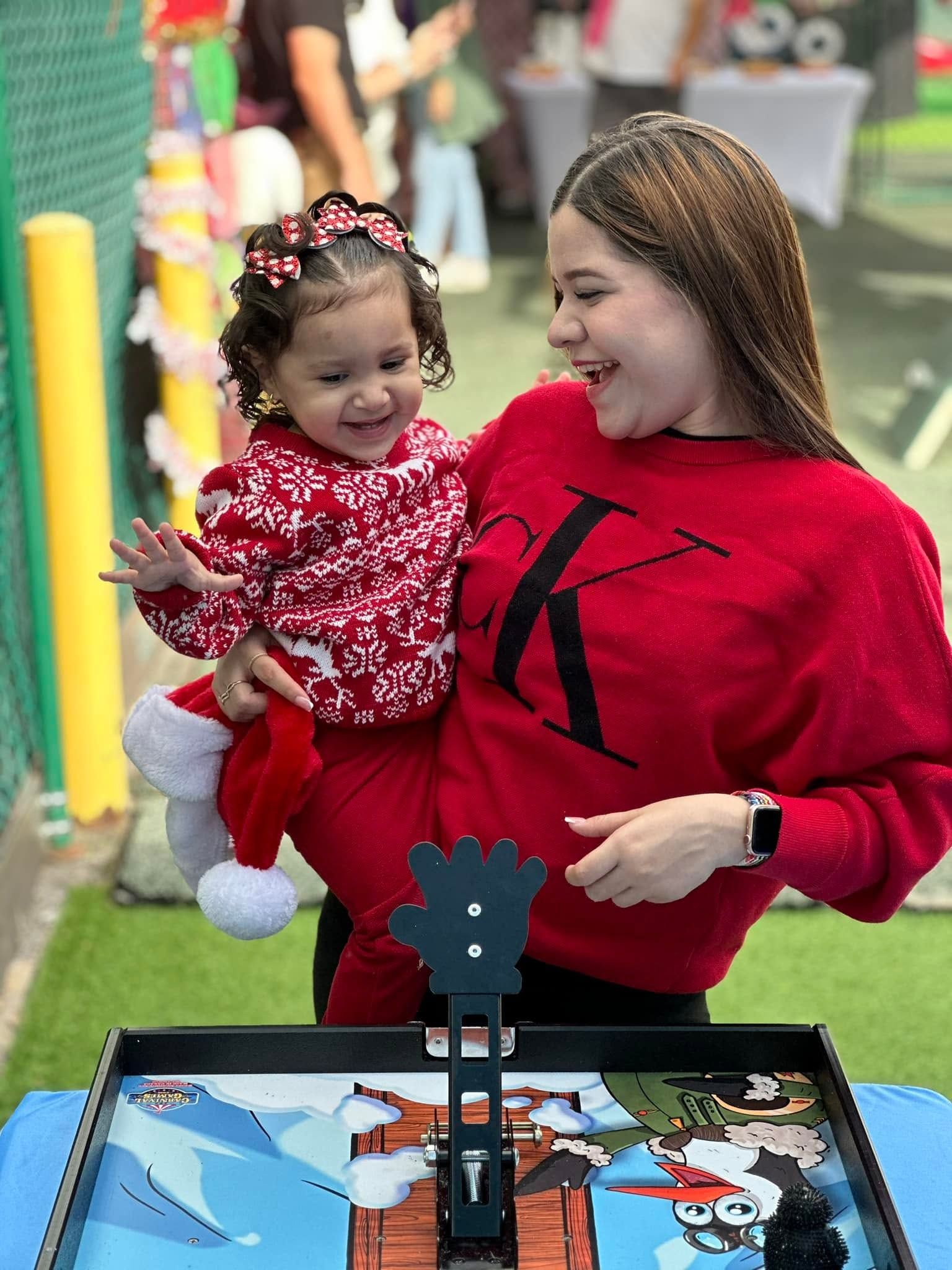 A mother helps a toddler in a holiday outfit play Penguin Flight School