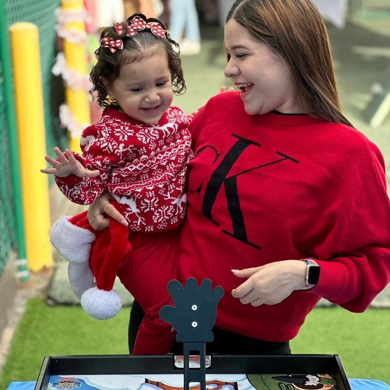 A mother helps a toddler in a holiday outfit play Penguin Flight School