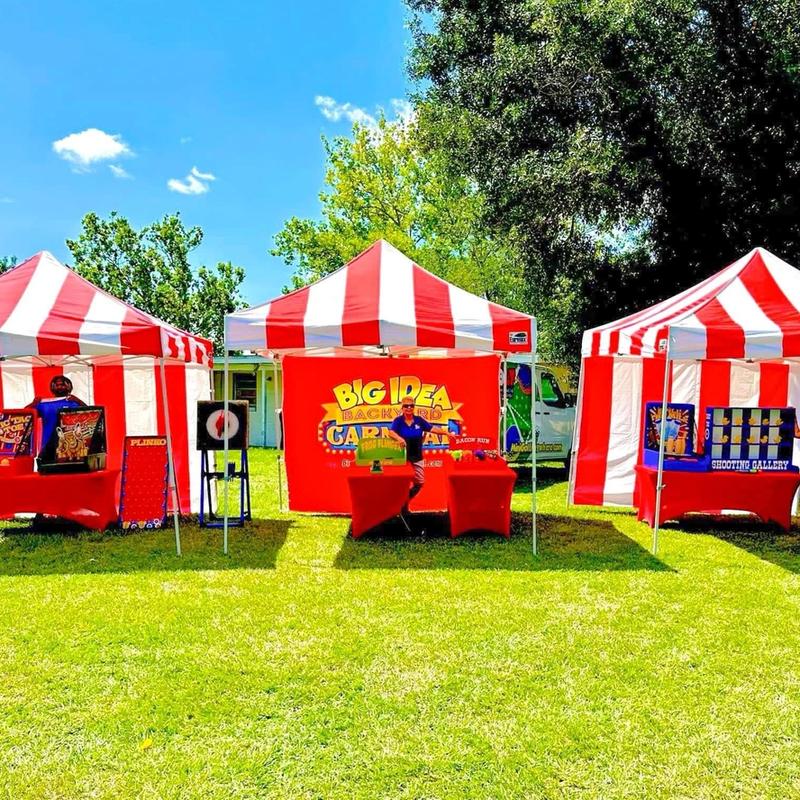 Three red and white striped tents setup with classic carnival games in preparation for a community festival.