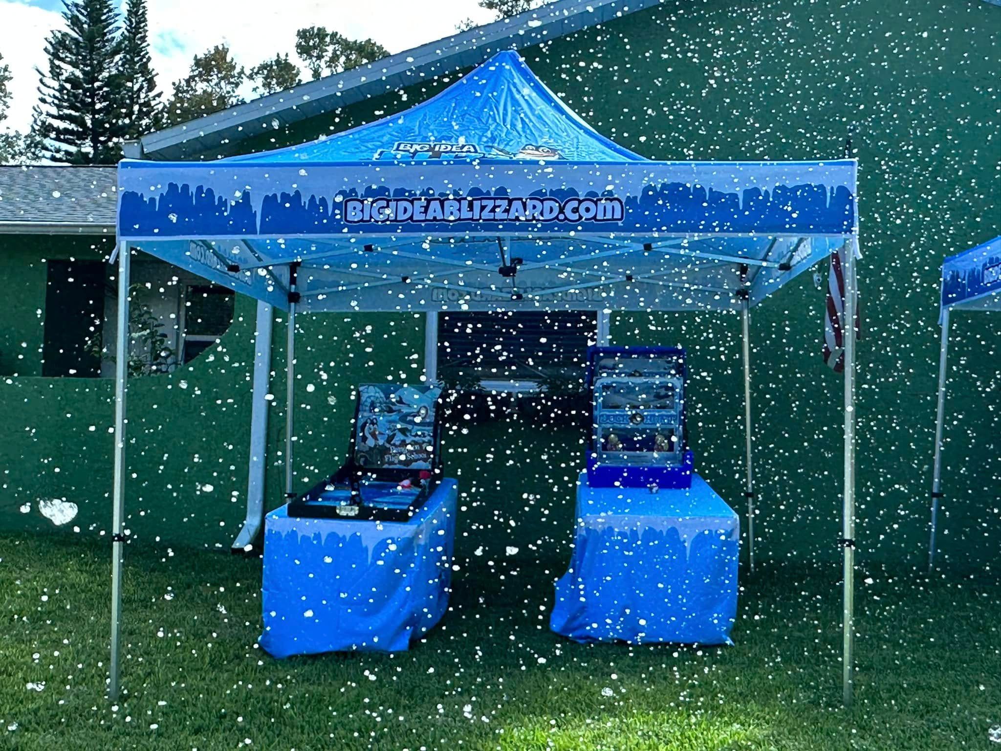 A Big Idea Blizzard tent over two game tables in heavy falling snow beside a house
