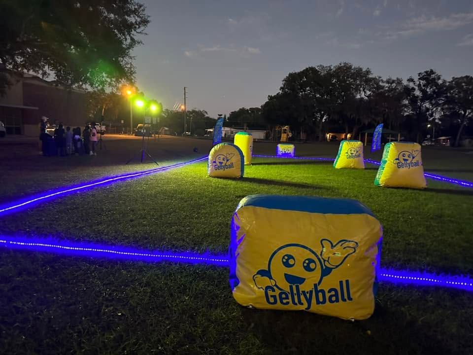 A gellyball field lit for a glow game at dusk, with inflatable bunkers and a lit boundary