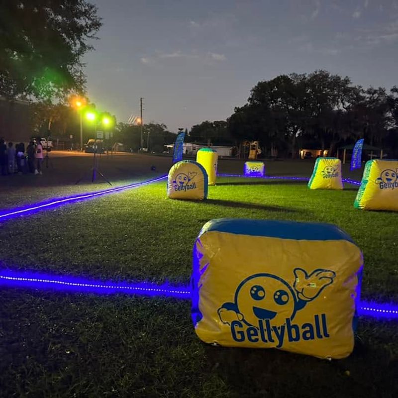 A gellyball field lit for a glow game at dusk, with inflatable bunkers and a lit boundary