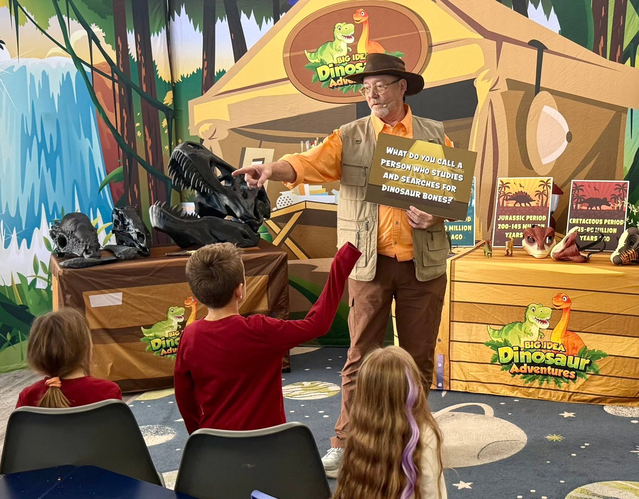 A presenter holding a question card in front of students at a Dinosaur Adventures show