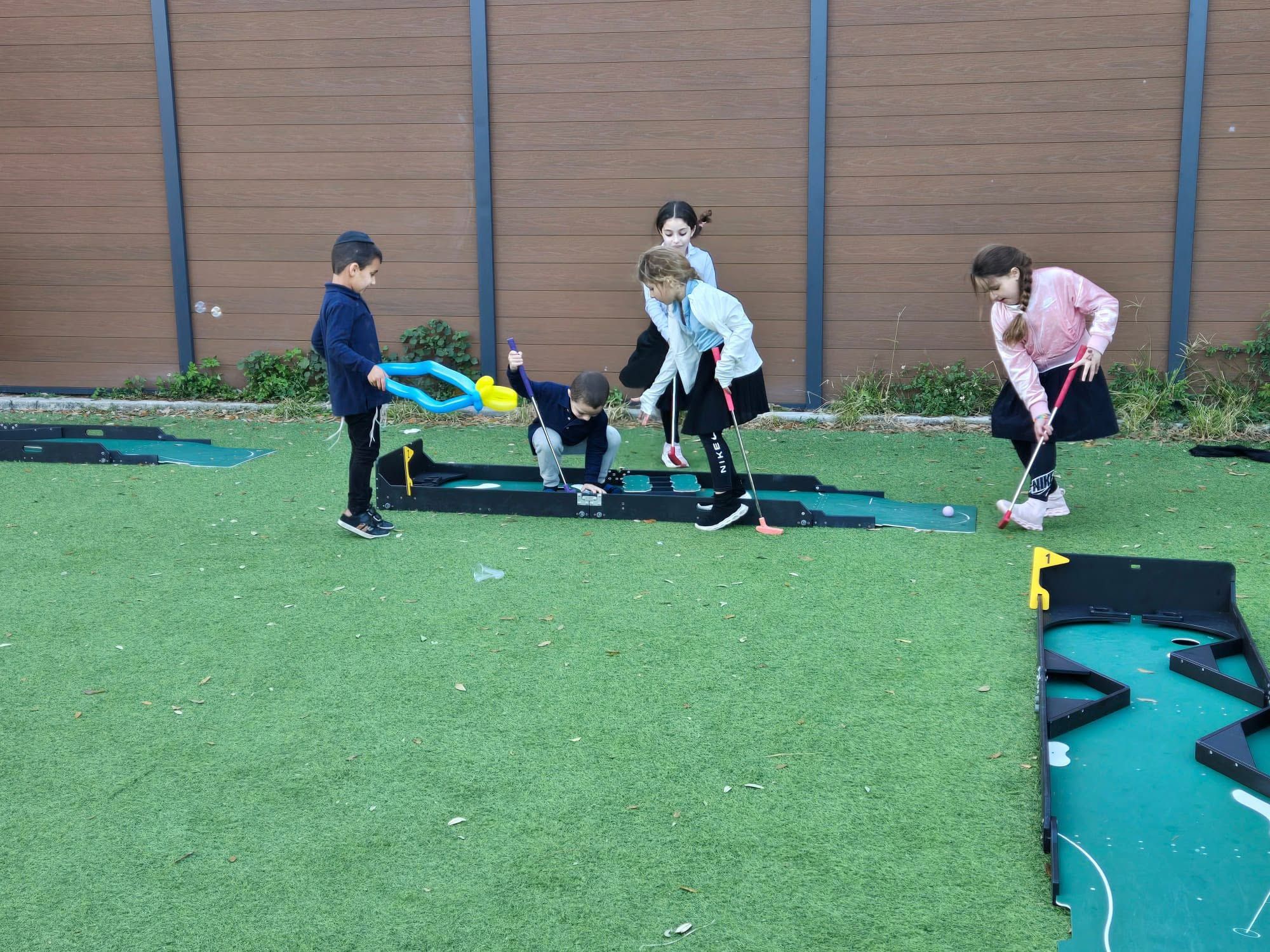 kids putting on a portable mini golf course set up on turf beside a sport court in Tampa