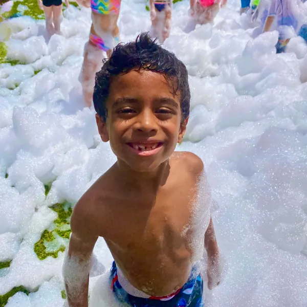 Kid smiling in a mountain of foam at a school foam party in Jacksonville