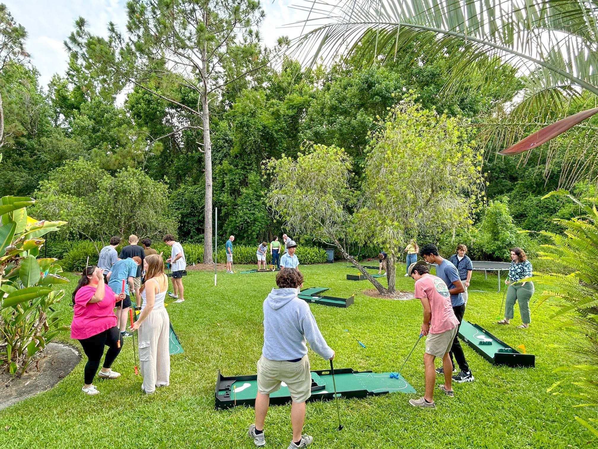 families playing several portable mini golf holes on a park lawn at a community event