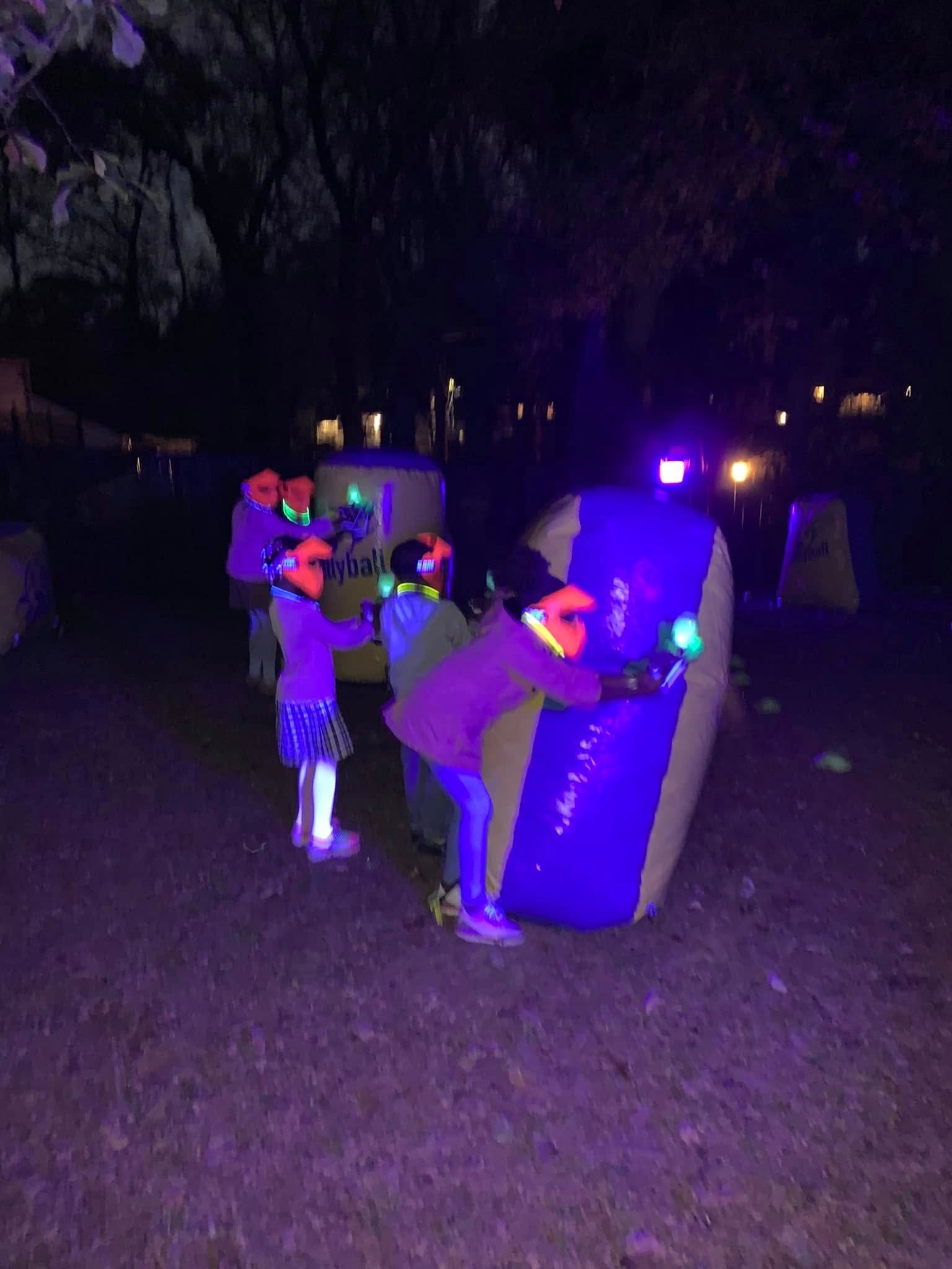Kids play a glow gellyball game at night behind a lit bunker