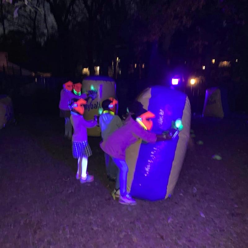 Kids play a glow gellyball game at night behind a lit bunker
