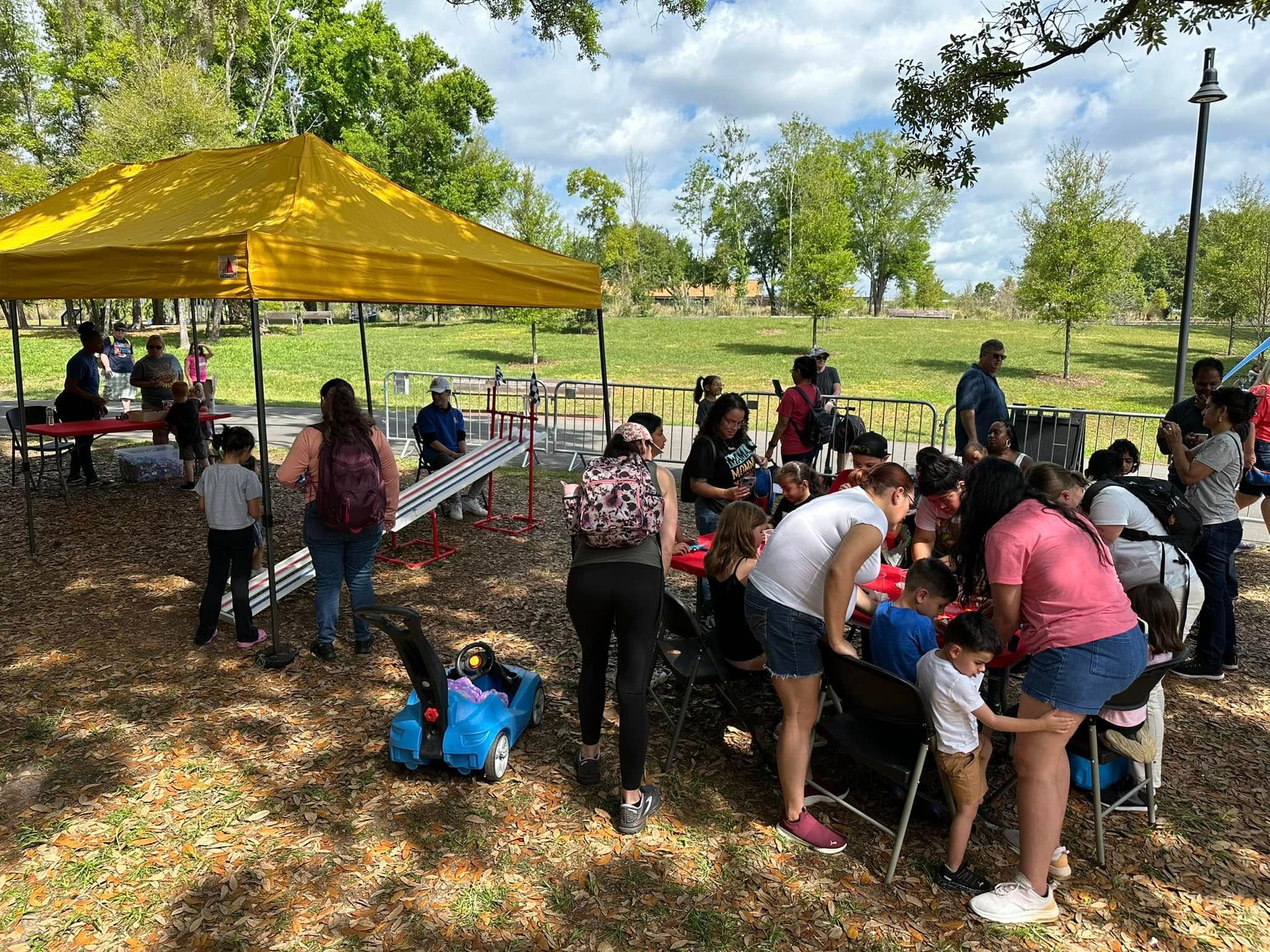 Kids and parents crowd a red build table while others race cars down the Derby ramp in a park