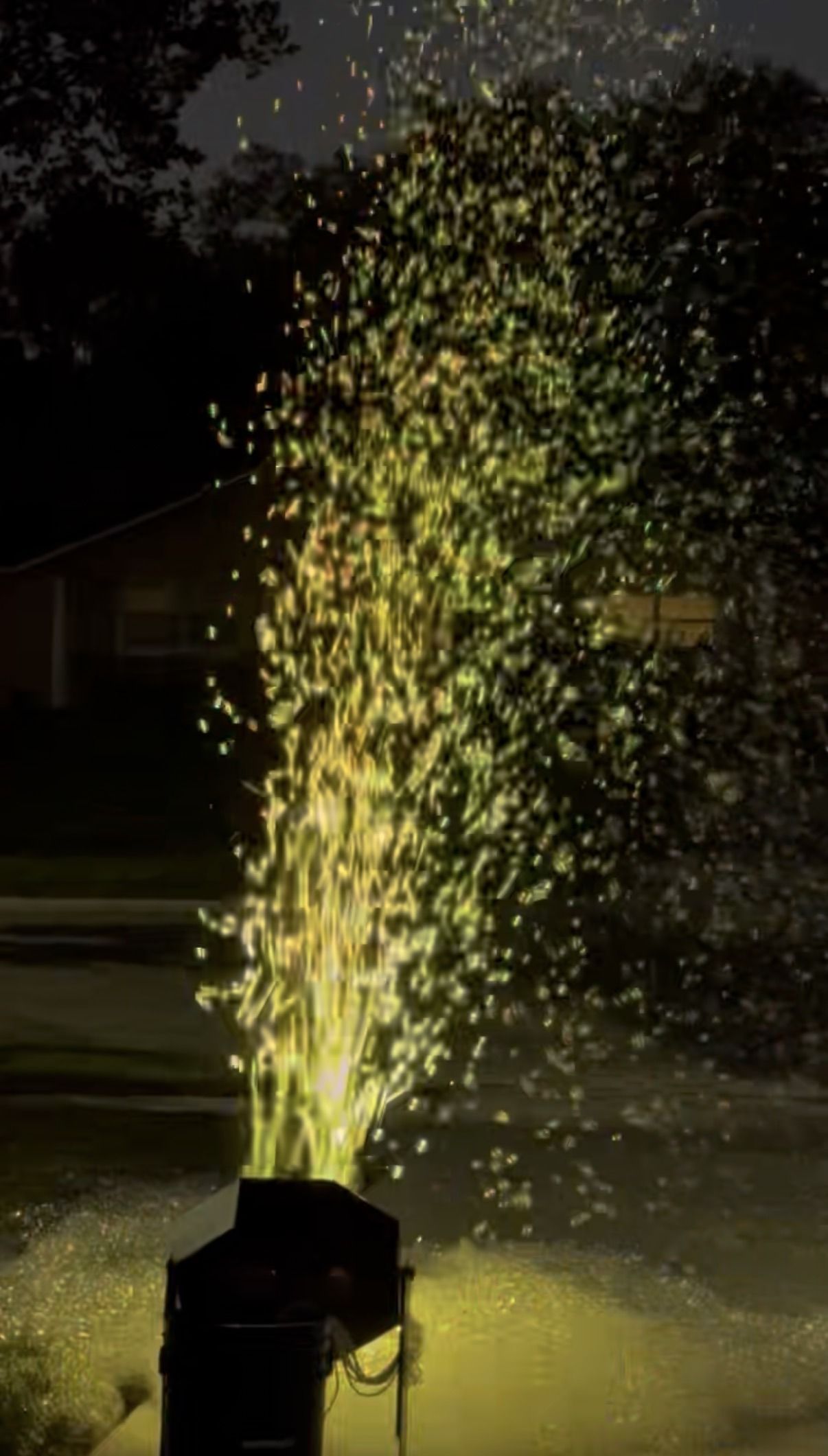 a bubble machine throwing a column of bubbles into the air on a lawn at night