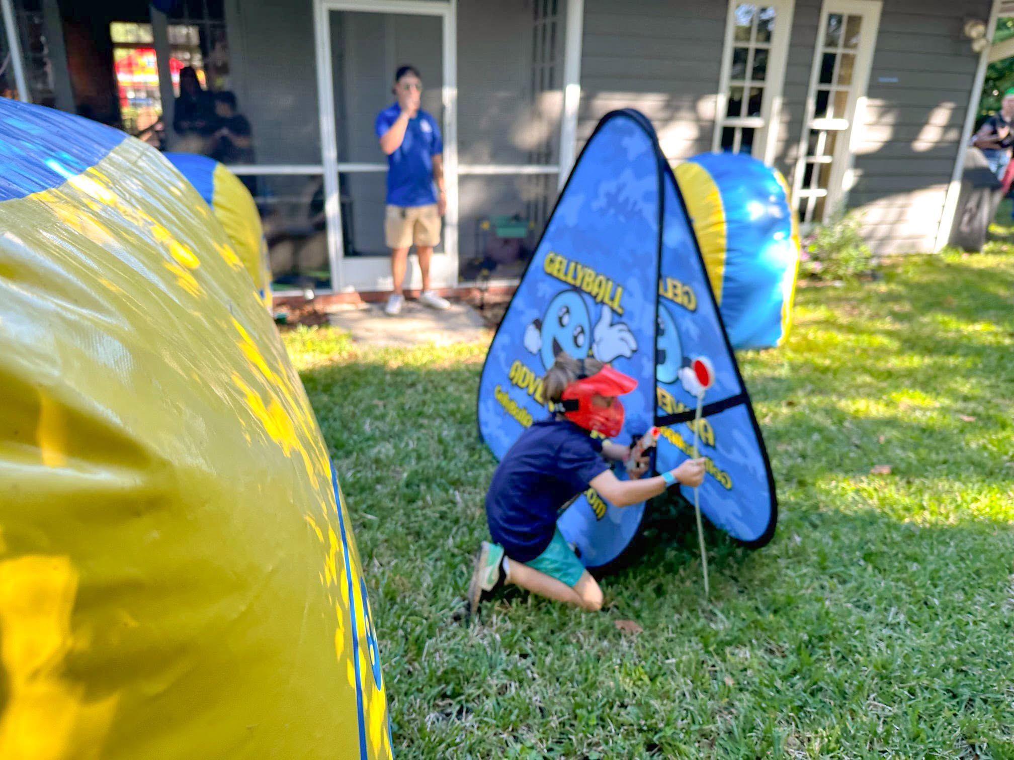 A child in a red mask kneels behind a pop-up bunker