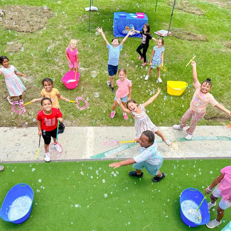 kids waving bubble wands on a turf lawn at a birthday party, seen from above