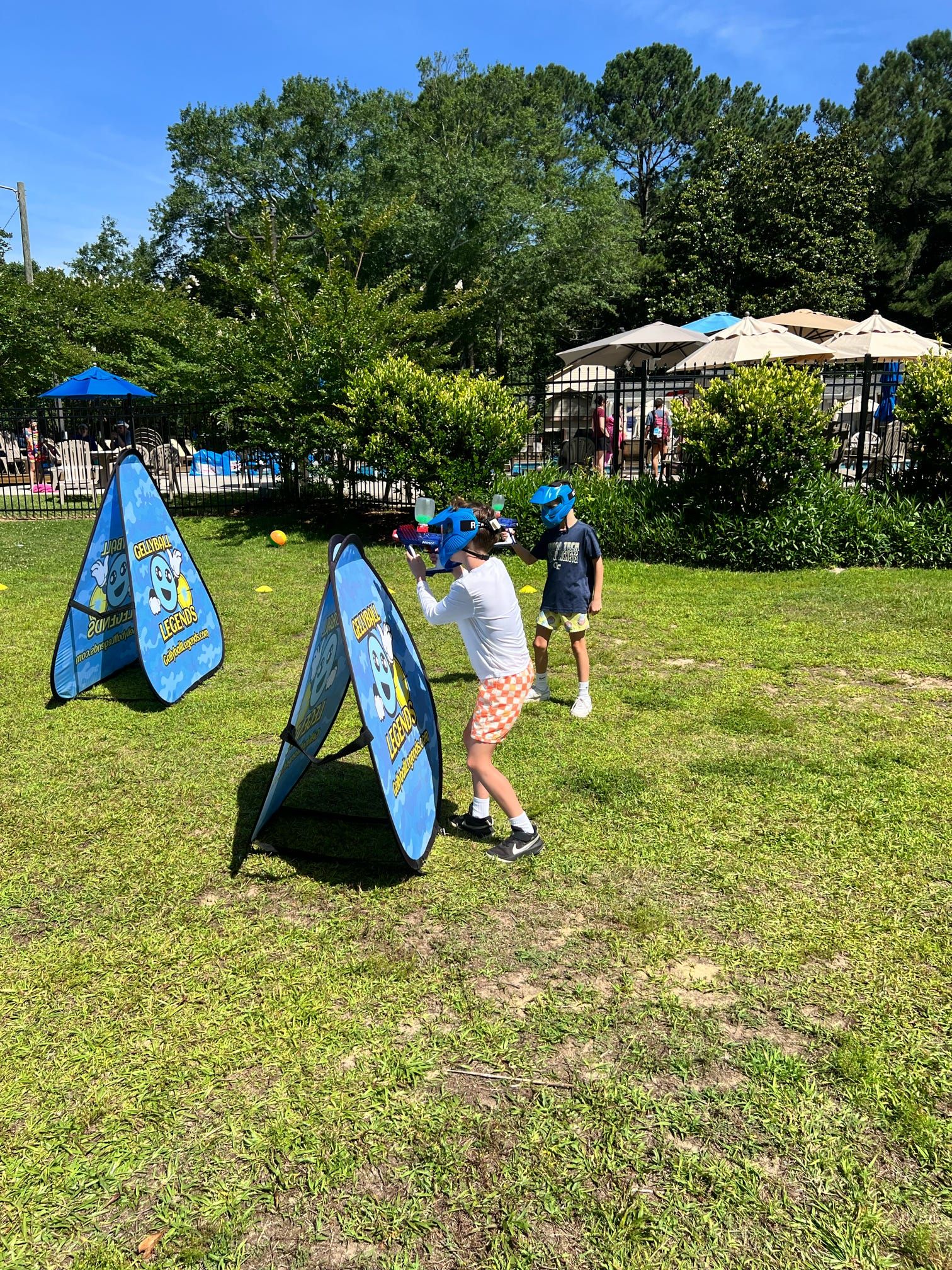 Two boys in blue masks play gellyball around A-frame bunkers on a lawn