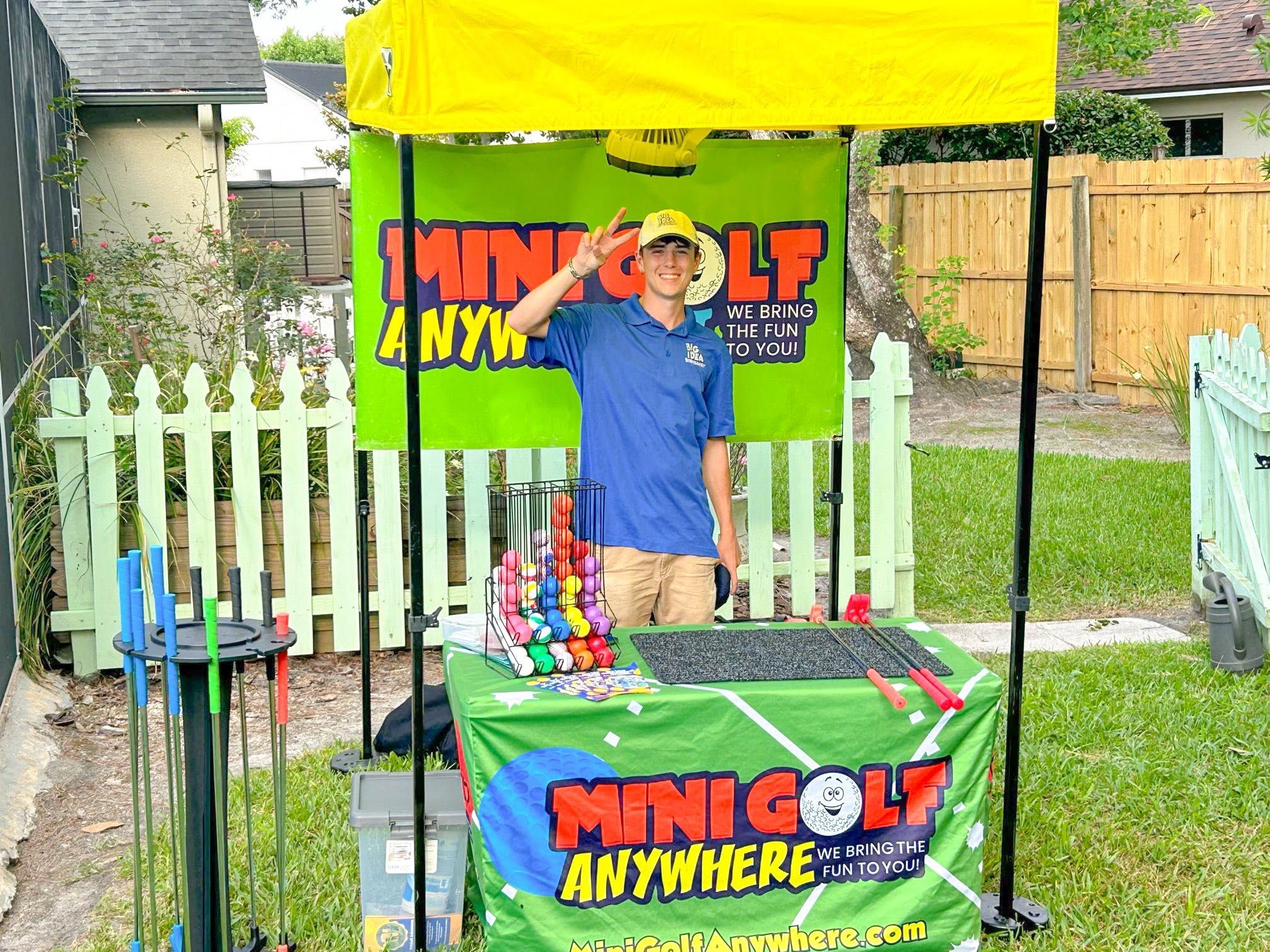 a staffer standing at the branded Mini Golf Anywhere canopy in a fenced backyard