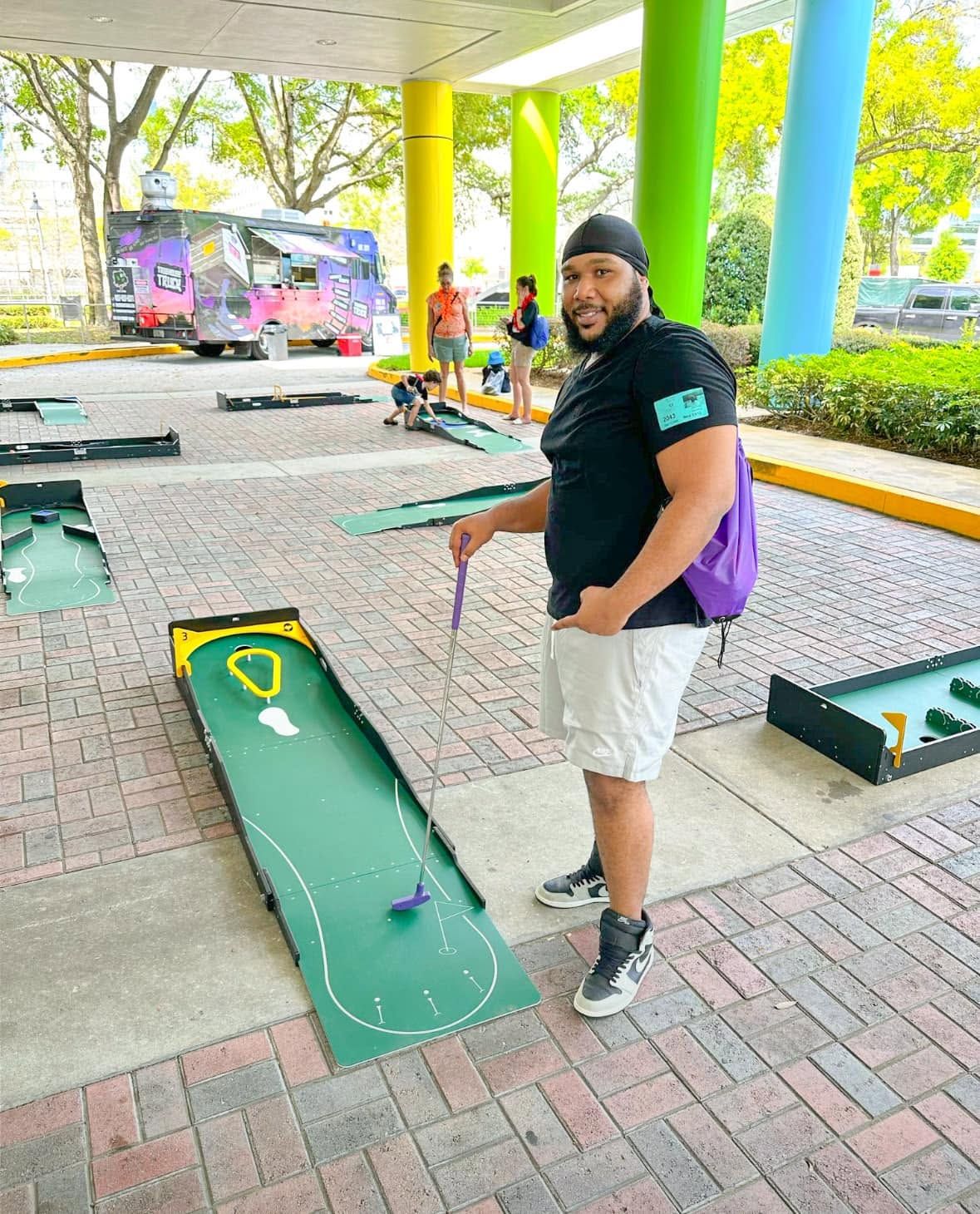 a staffer beside a portable mini golf hole set up on a brick patio