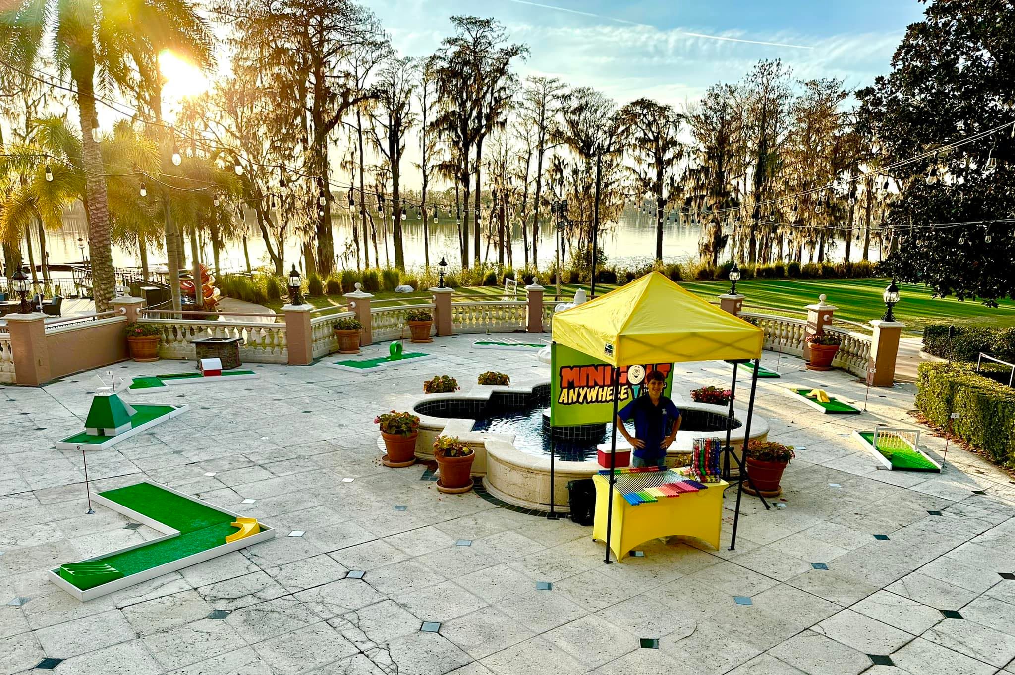 a full portable mini golf course set up across a paved courtyard with palm trees and a shade canopy