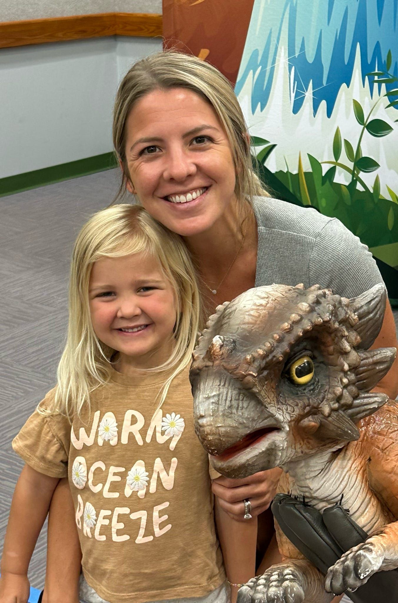 A smiling girl and her mom pose with a lifelike baby dinosaur