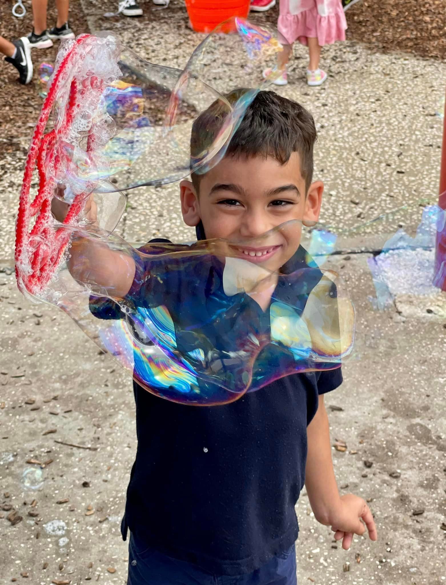 a smiling boy leaning into a giant bubble held on a wand