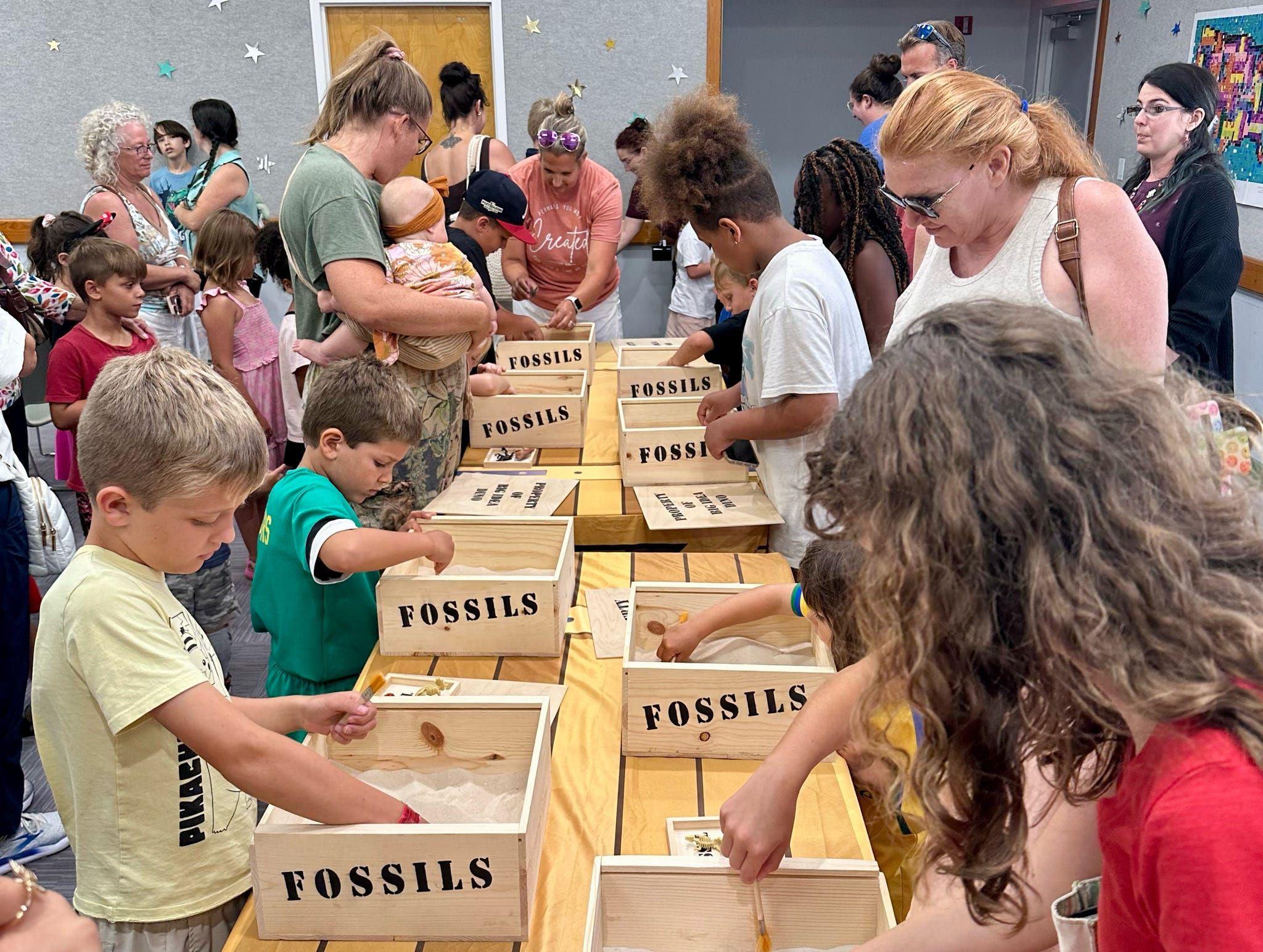 Kids and parents work a long table of fossil dig boxes