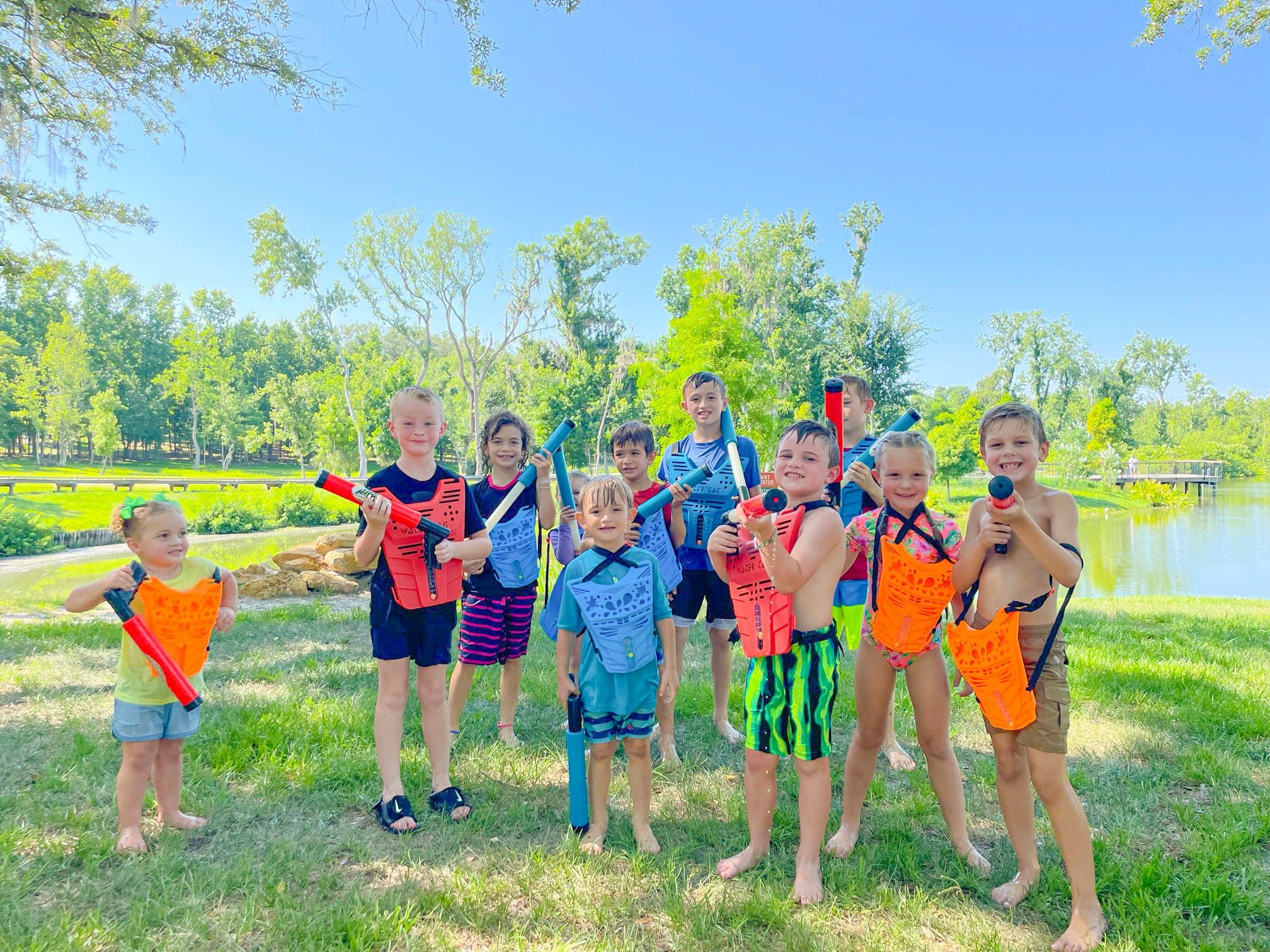 A group of kids in water vests poses with their blasters by a lake