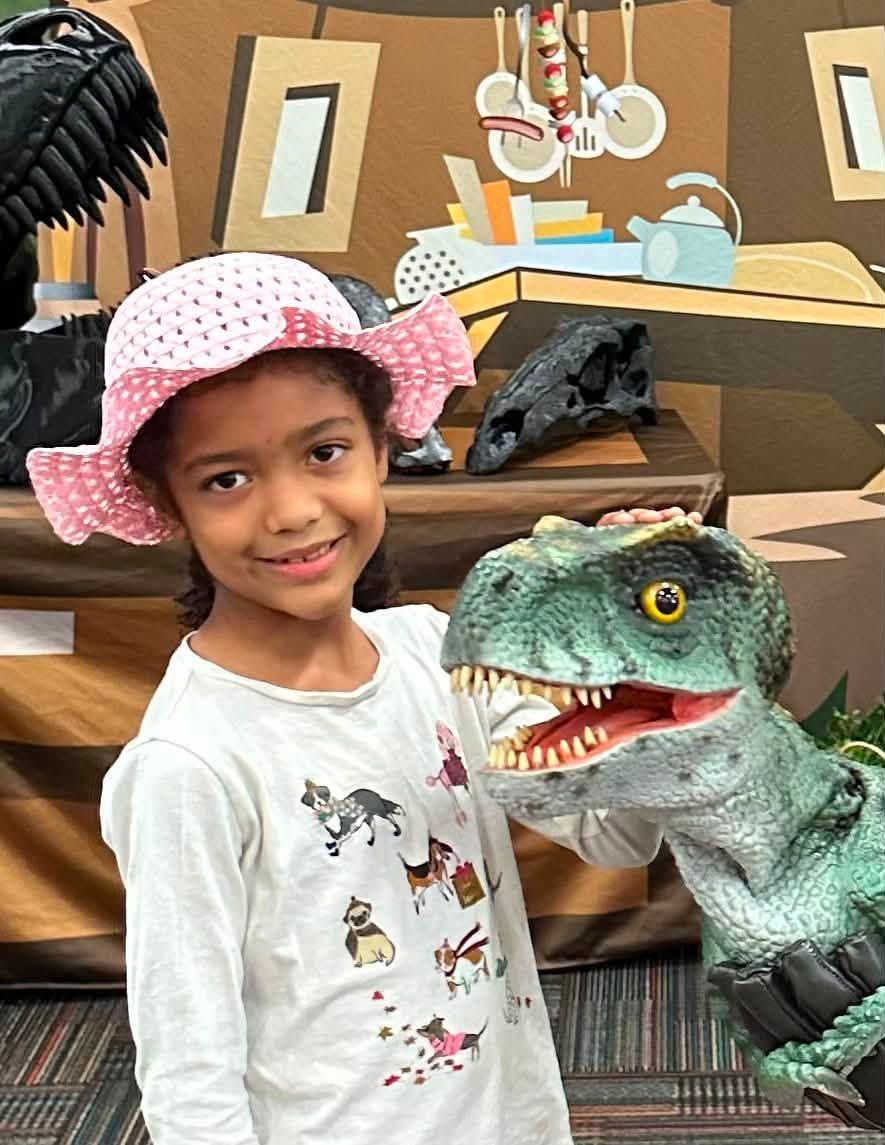 A girl in a pink sun hat smiles beside a lifelike baby T. rex