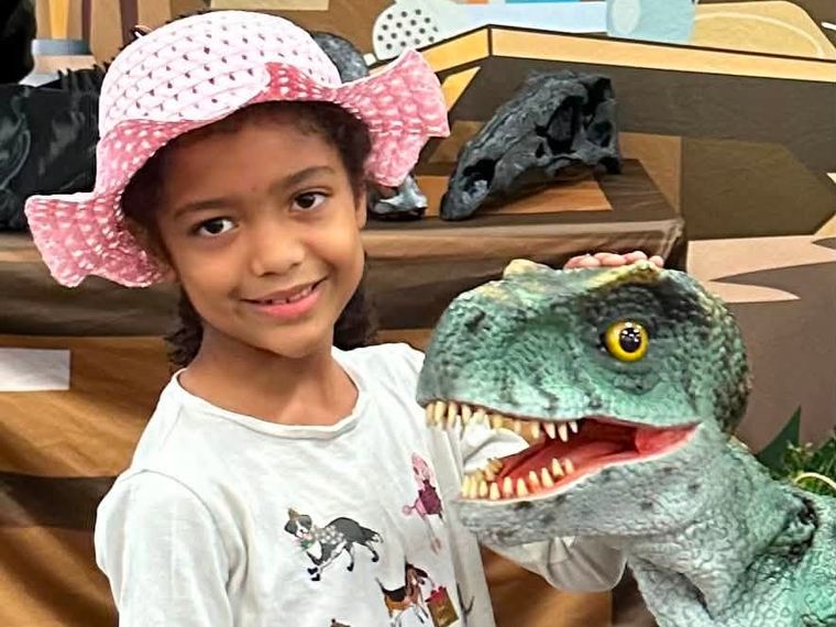 A girl in a pink sun hat smiles beside a lifelike baby T. rex