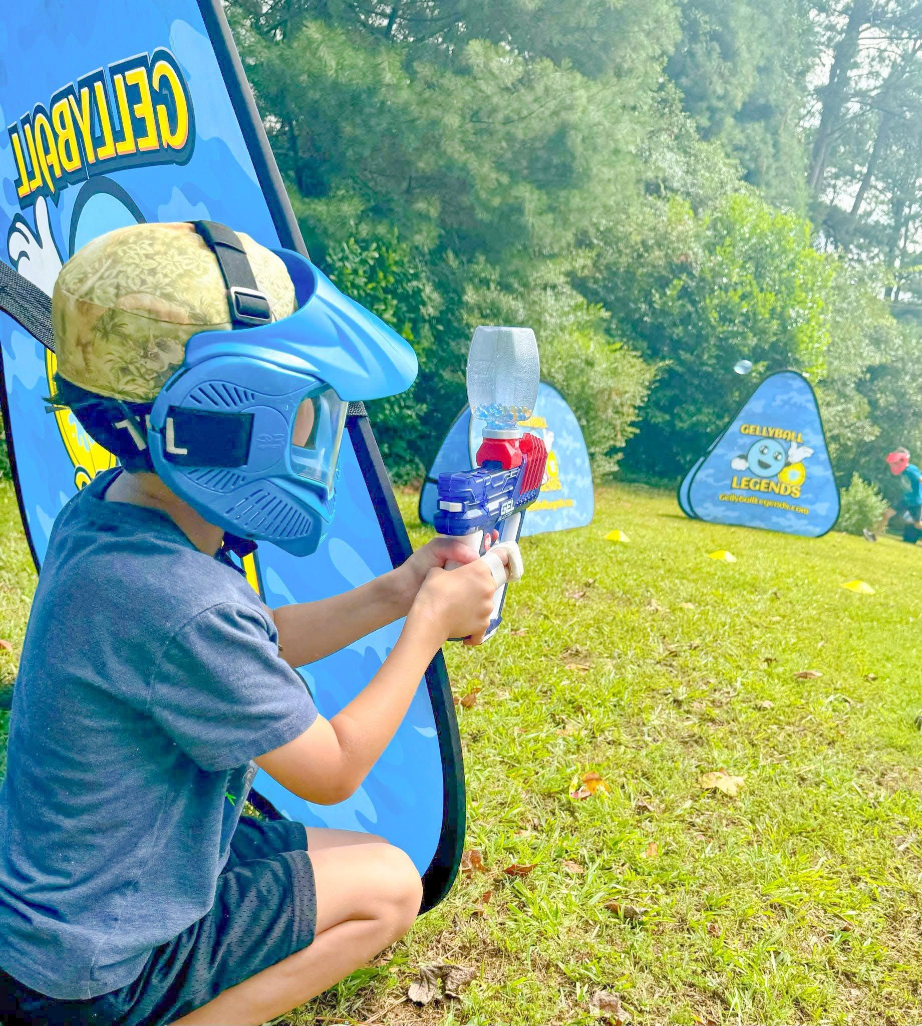 A boy in a blue mask aims from behind a pop-up bunker at the edge of the woods