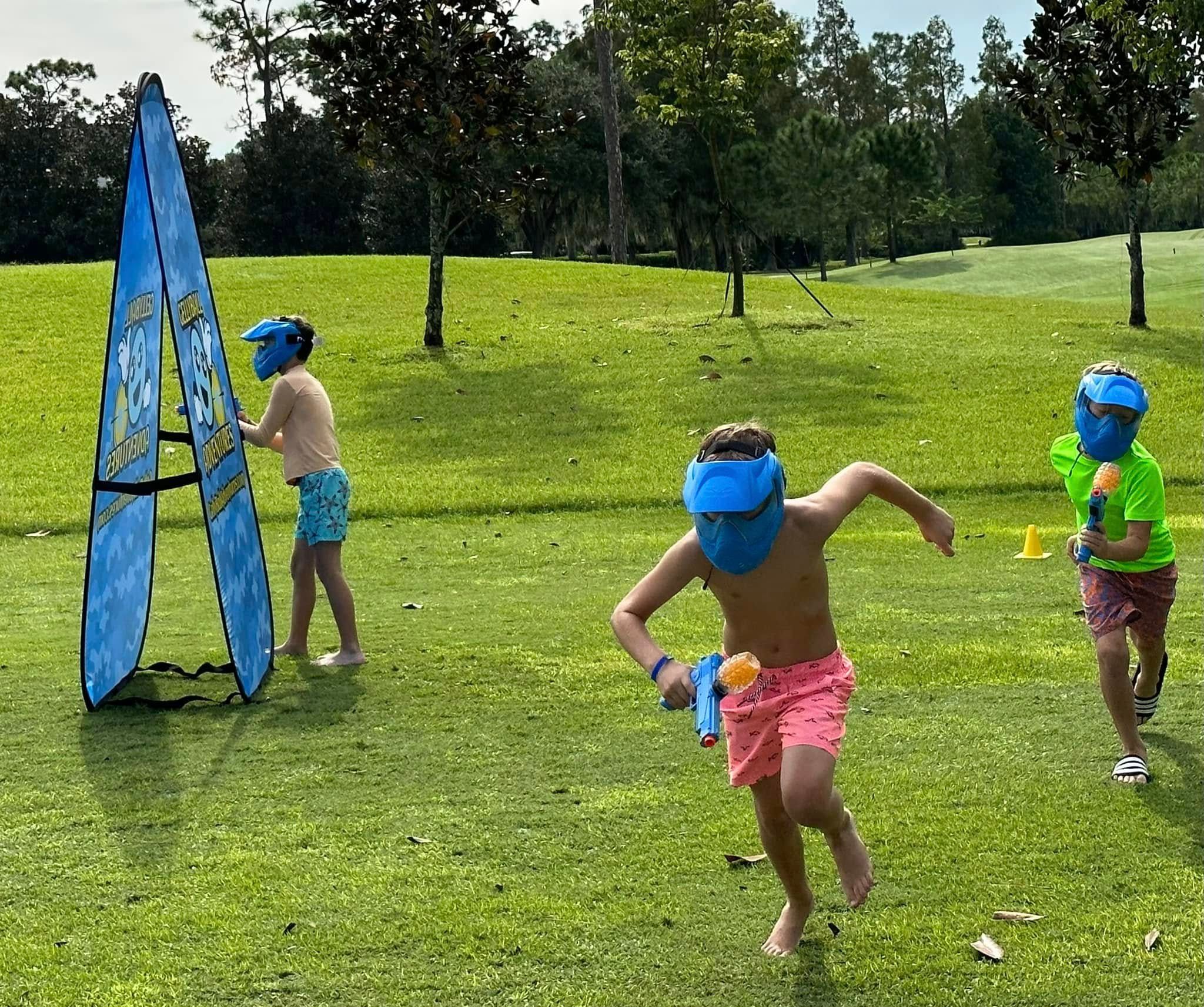 A boy in a mask runs across a lawn during a gellyball game