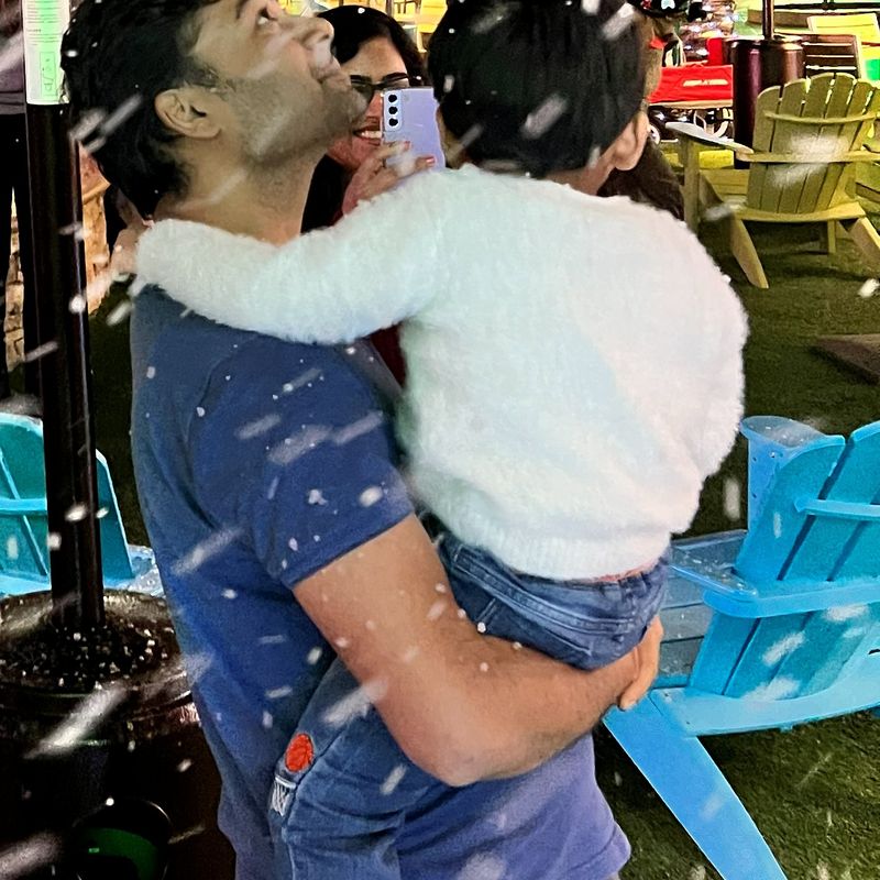 A child in a parent's arms looks up as snow falls at a holiday night event